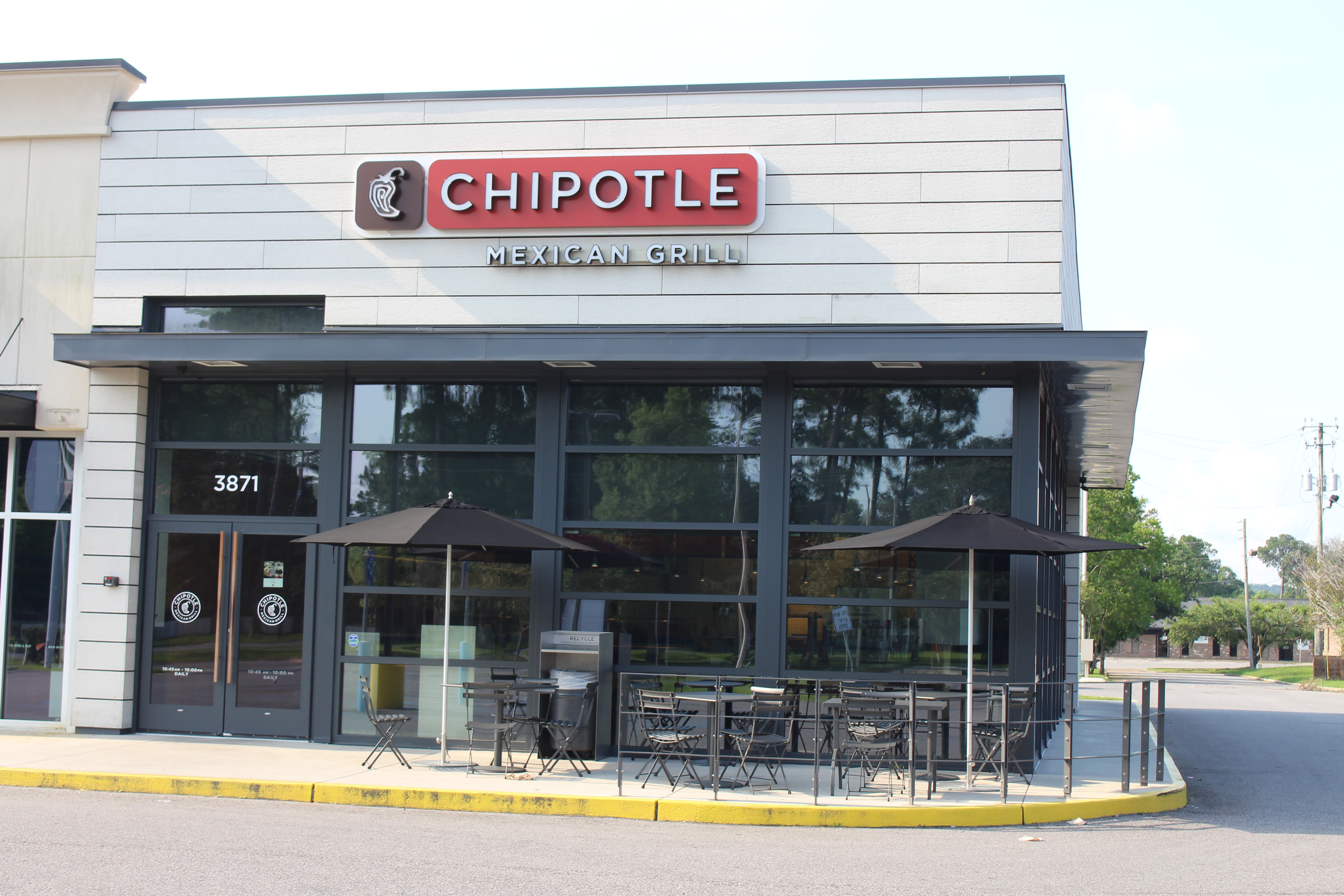Exterior of a Chipotle Mexican Grill restaurant with outdoor patio seating and black umbrellas.