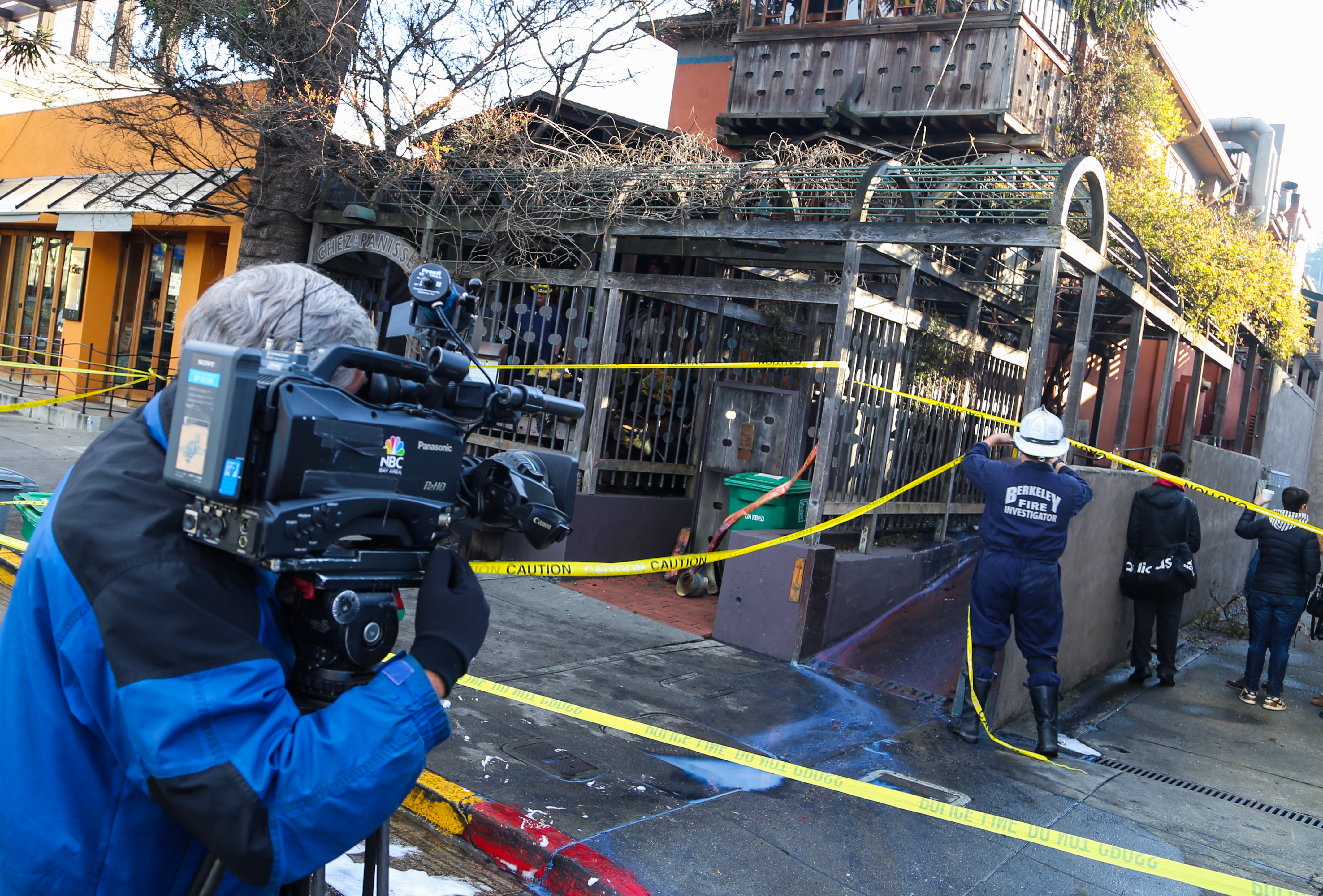 Yellow caution tape blocks a restaurant entrance as investigators stand nearby.