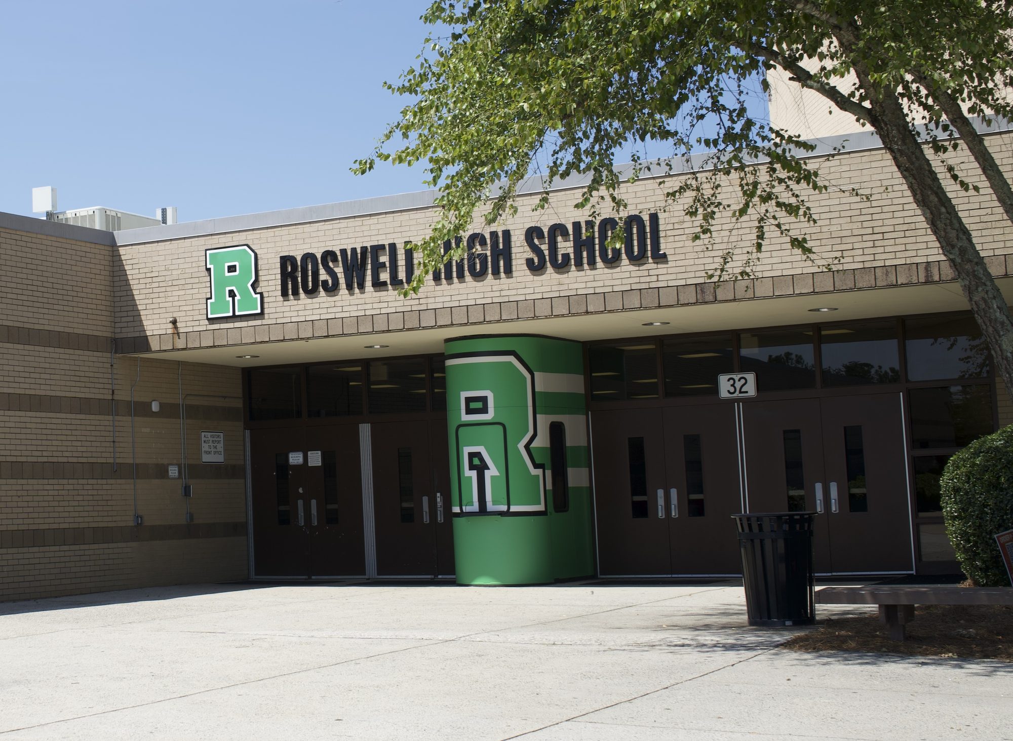 Brick high school entrance with large green letter logo above glass doors