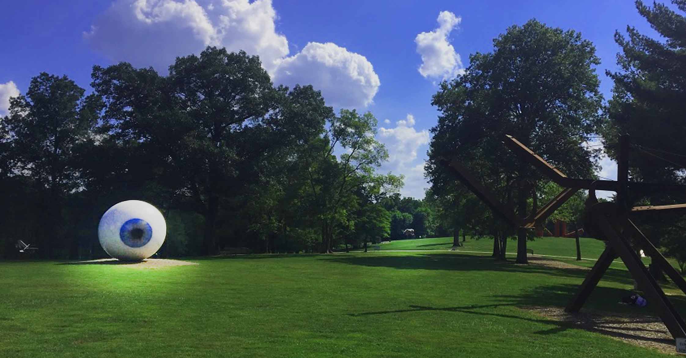 Large white eyeball sculpture on a grassy lawn surrounded by trees at an outdoor sculpture park.