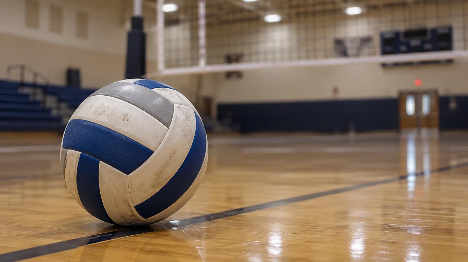 A volleyball sitting on a hardwood gym floor near a volleyball net.