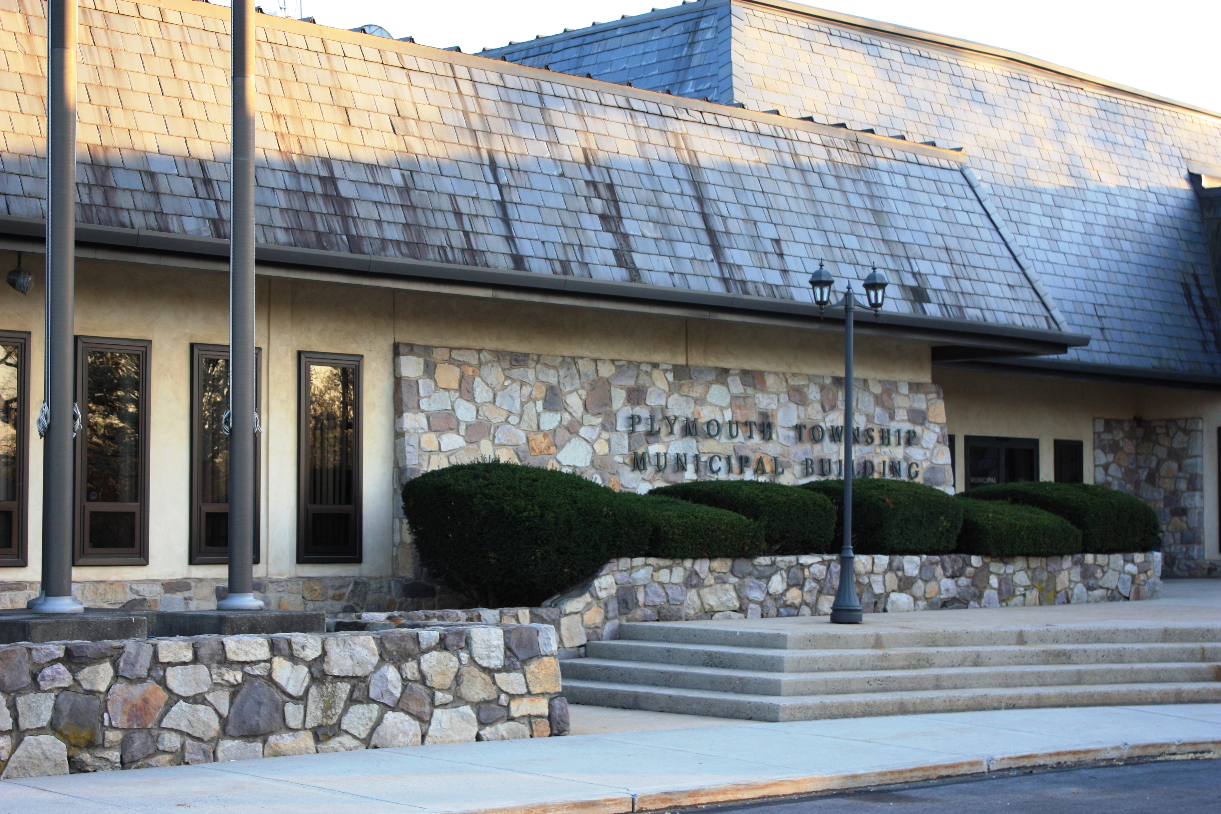 Stone entrance of a municipal building with metal lettering and trimmed hedges.