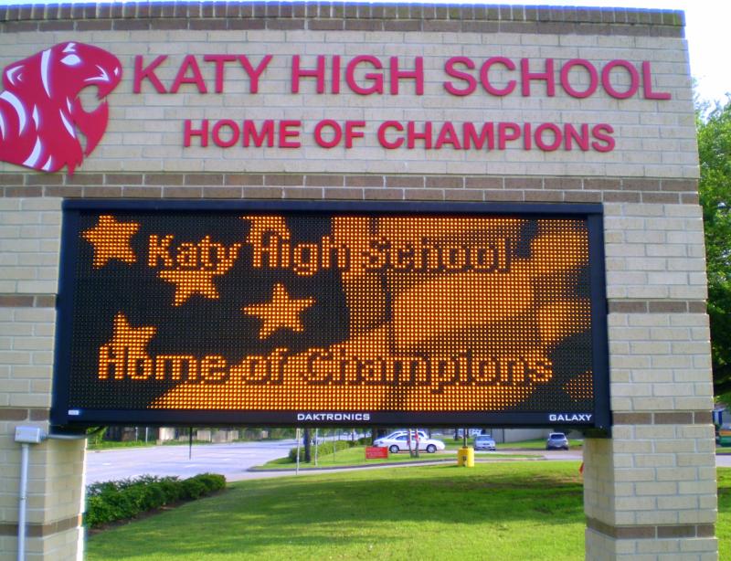 Brick school sign reading 'Katy High School – Home of Champions' with LED marquee.