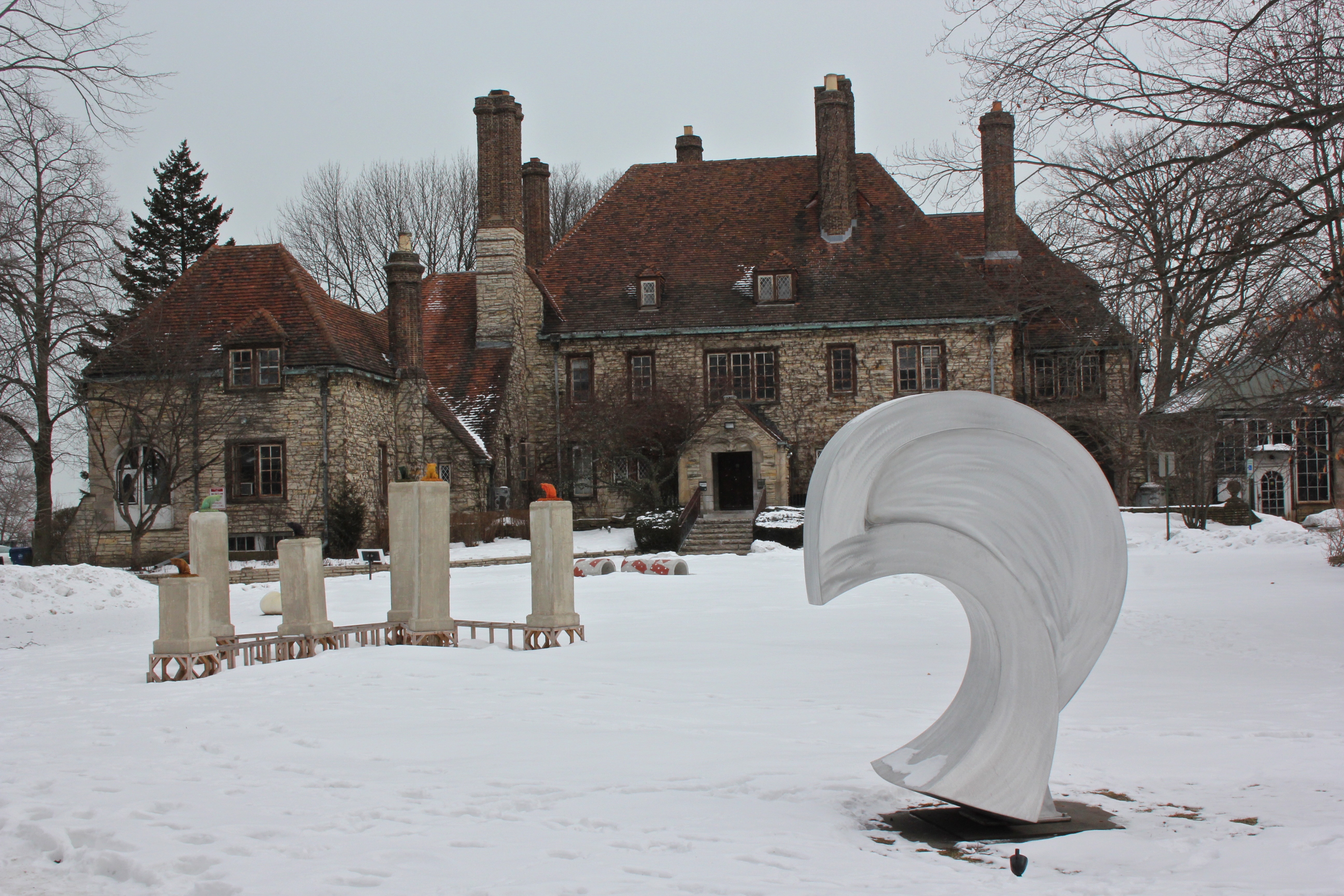 Stone manor-style building with red tile roof and white sculptures on a snowy lawn.