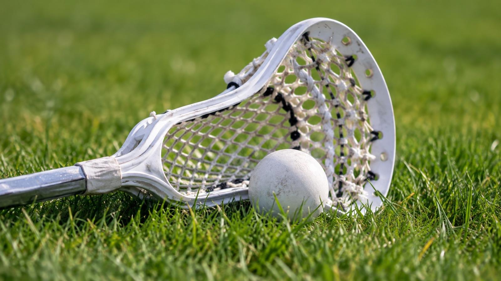 A lacrosse stick and rubber ball resting on green grass.