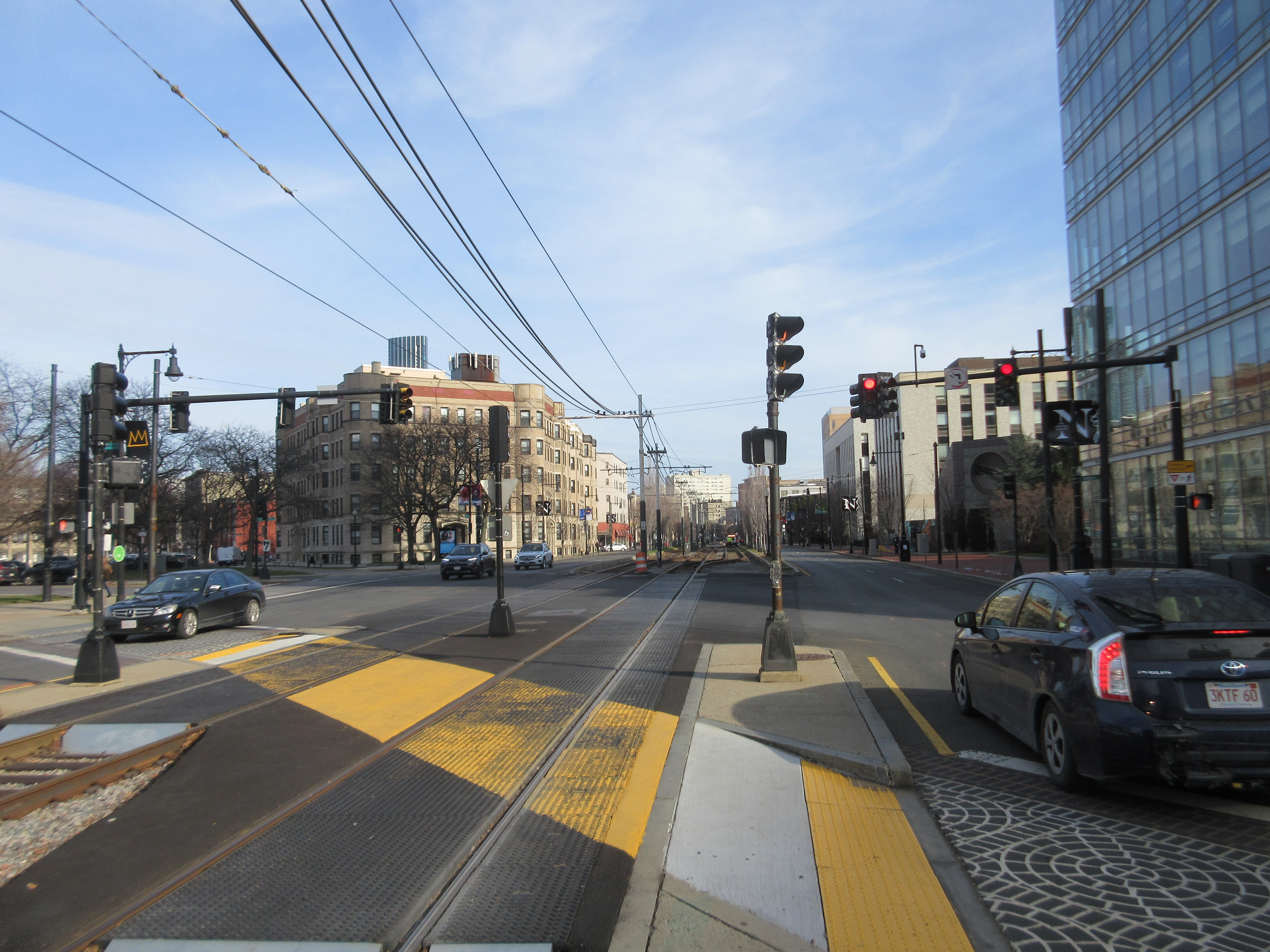 Light rail tracks cross a city street intersection with overhead catenary wires above.