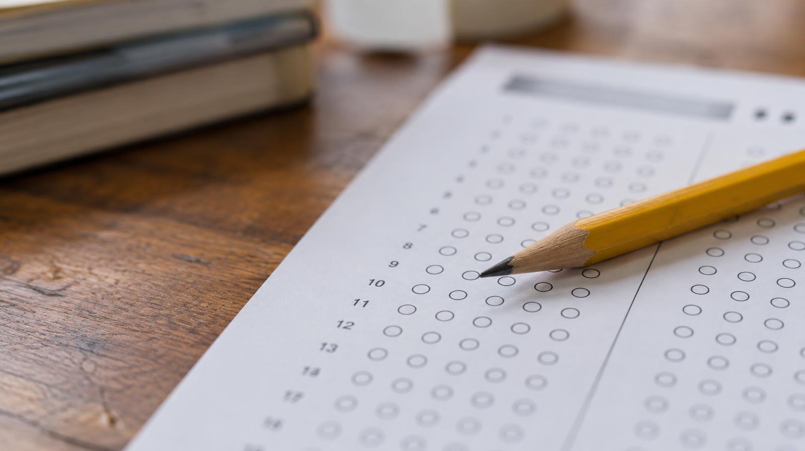 A sharpened pencil resting on a blank standardized test answer sheet with rows of empty bubbles.