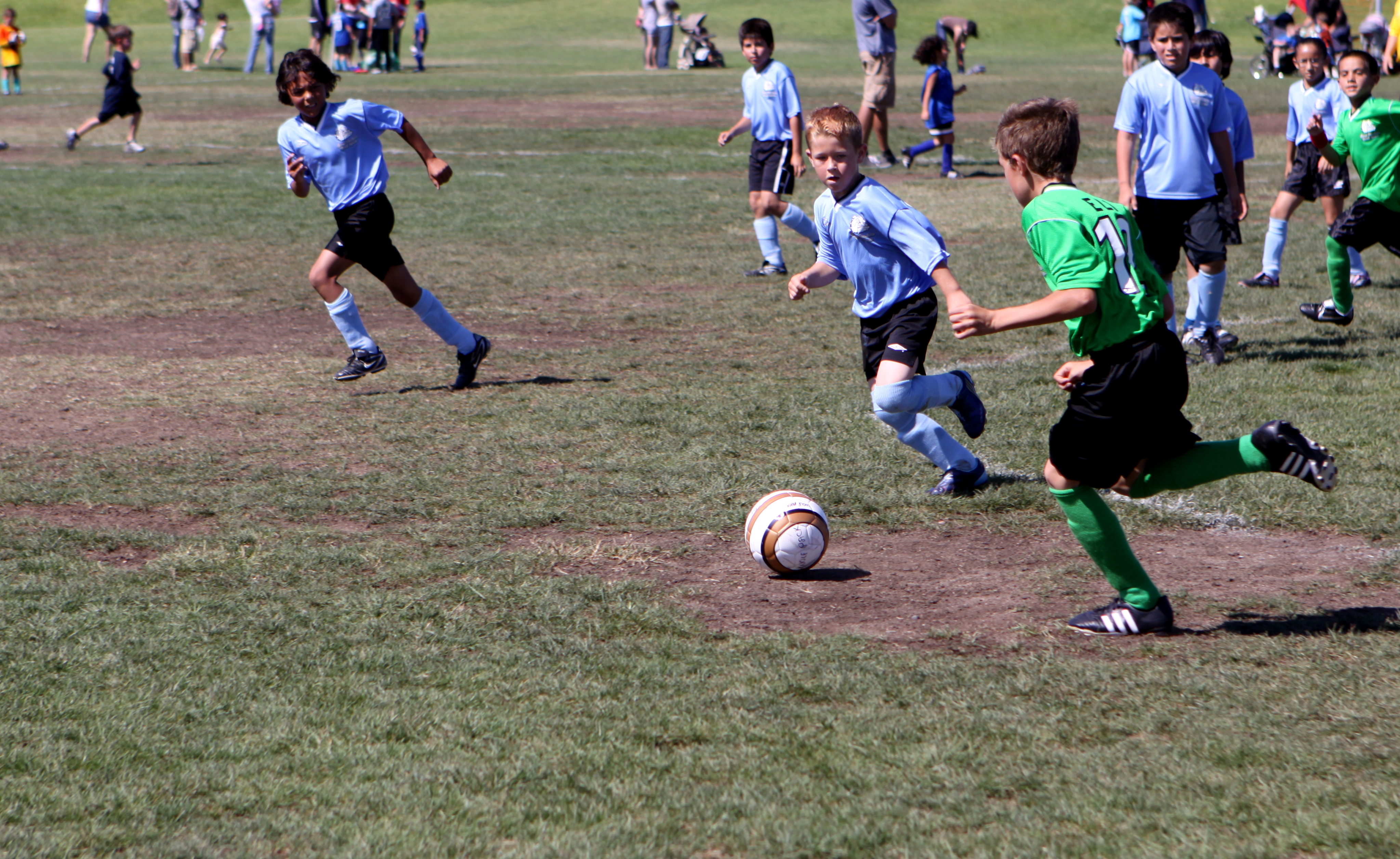 Children in blue and green jerseys playing soccer on a grass field during a youth league game.
