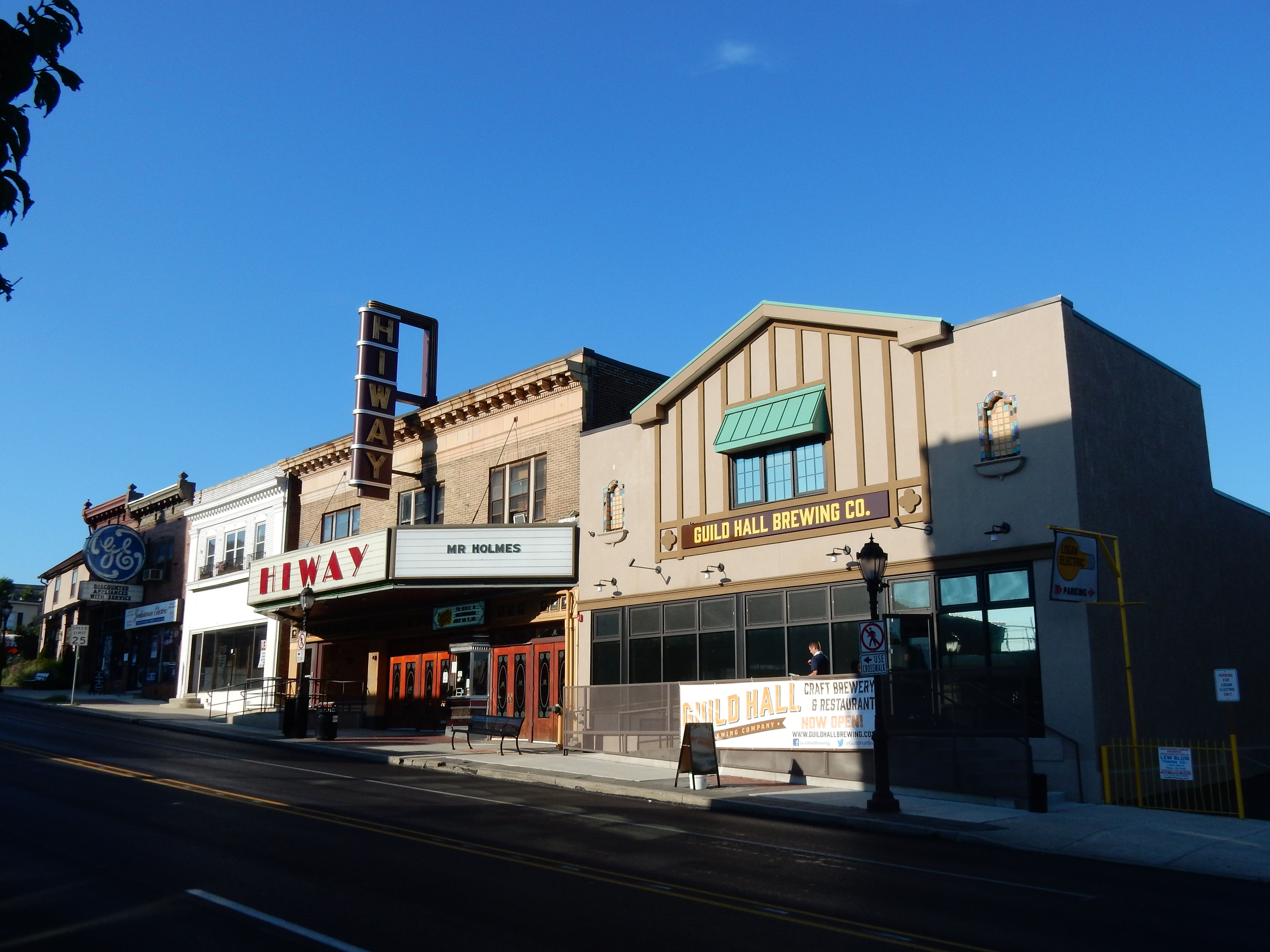 Street-level view of a theater marquee with vertical sign and neighboring storefronts.