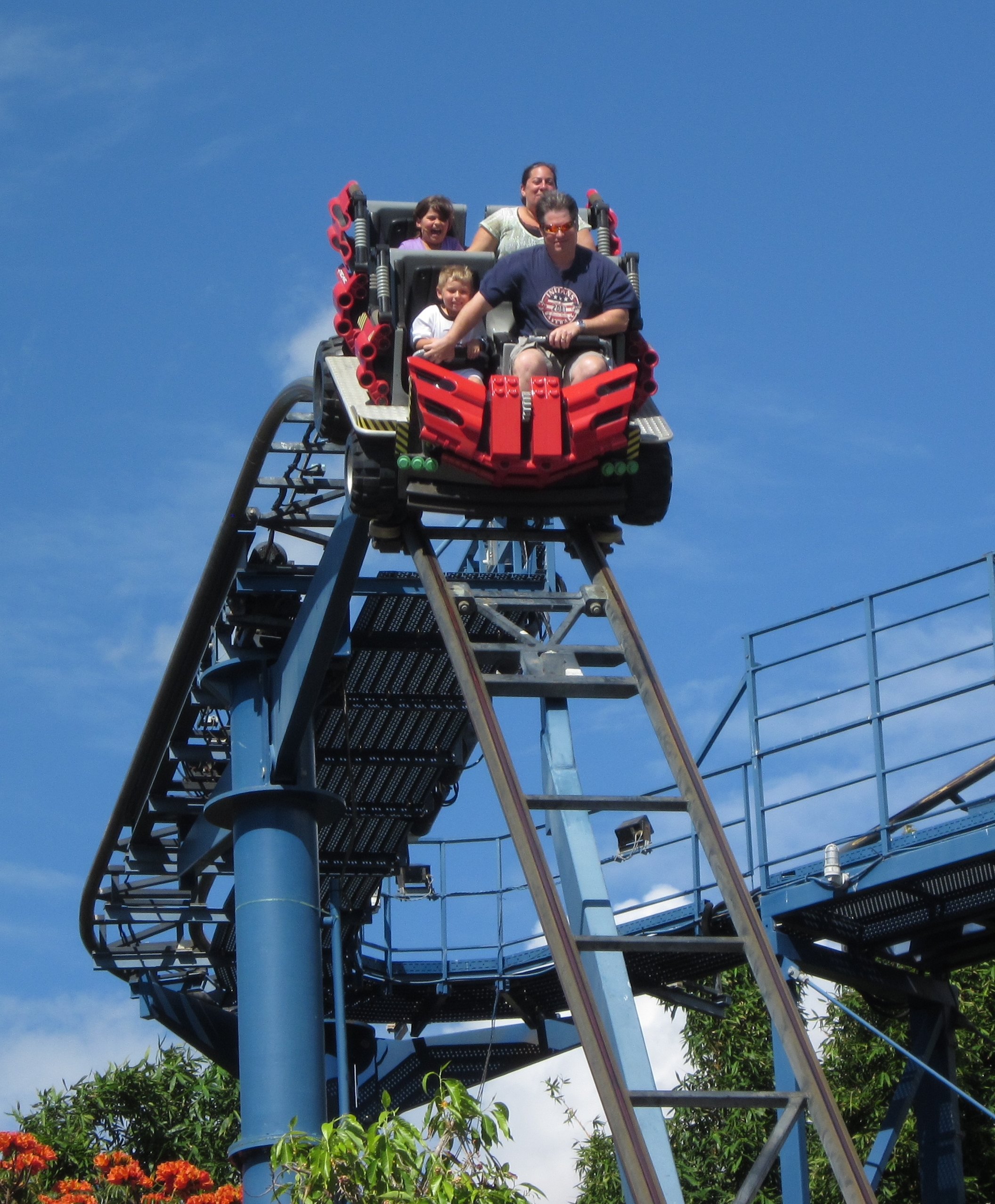 Four riders on a red roller coaster car cresting a lift hill at Legoland California.