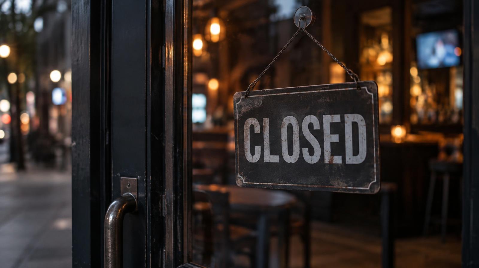 A closed sign hanging on the glass door of a dimly lit bar.