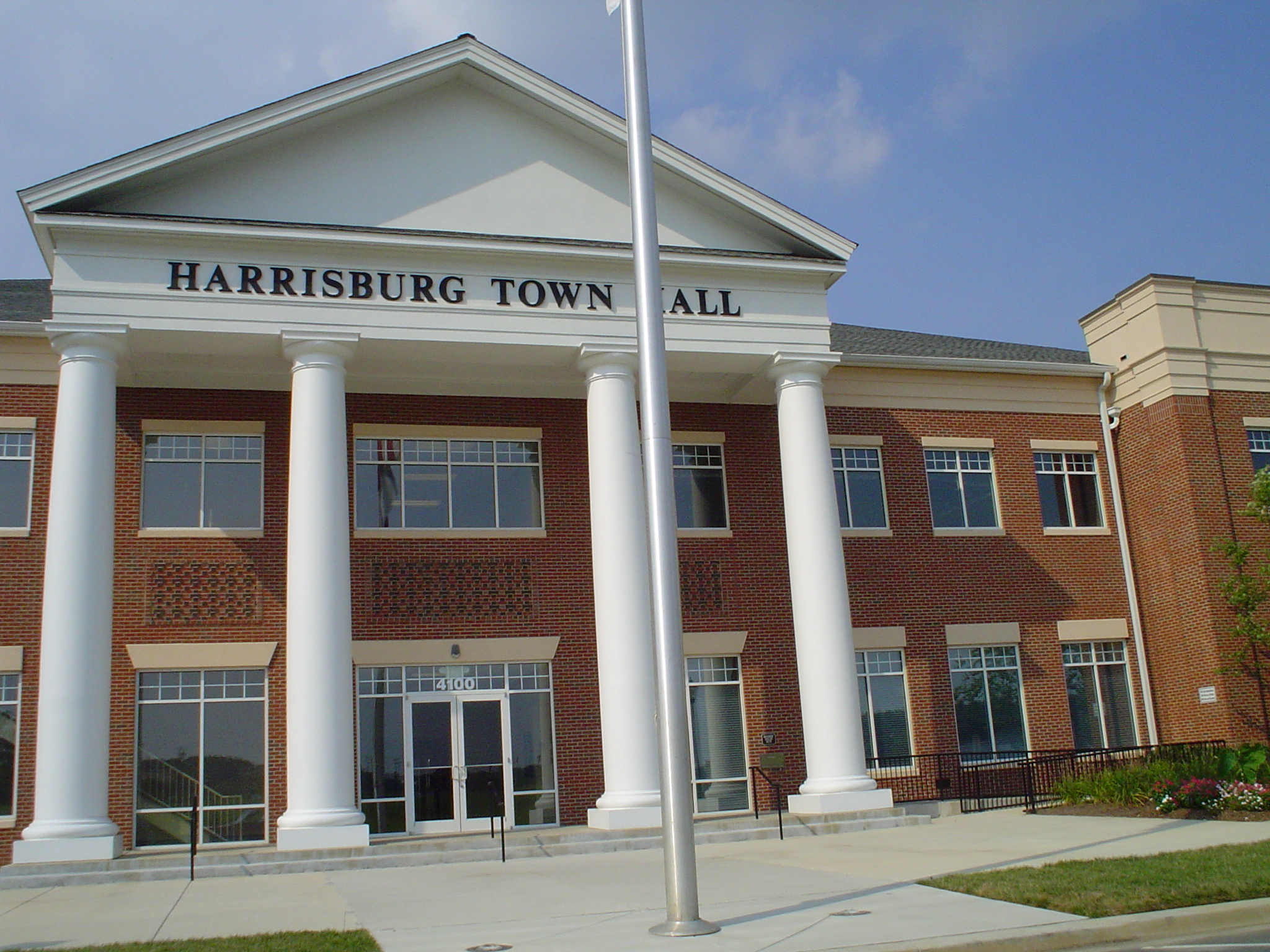 Two-story red brick town hall with white columns and a flagpole out front.