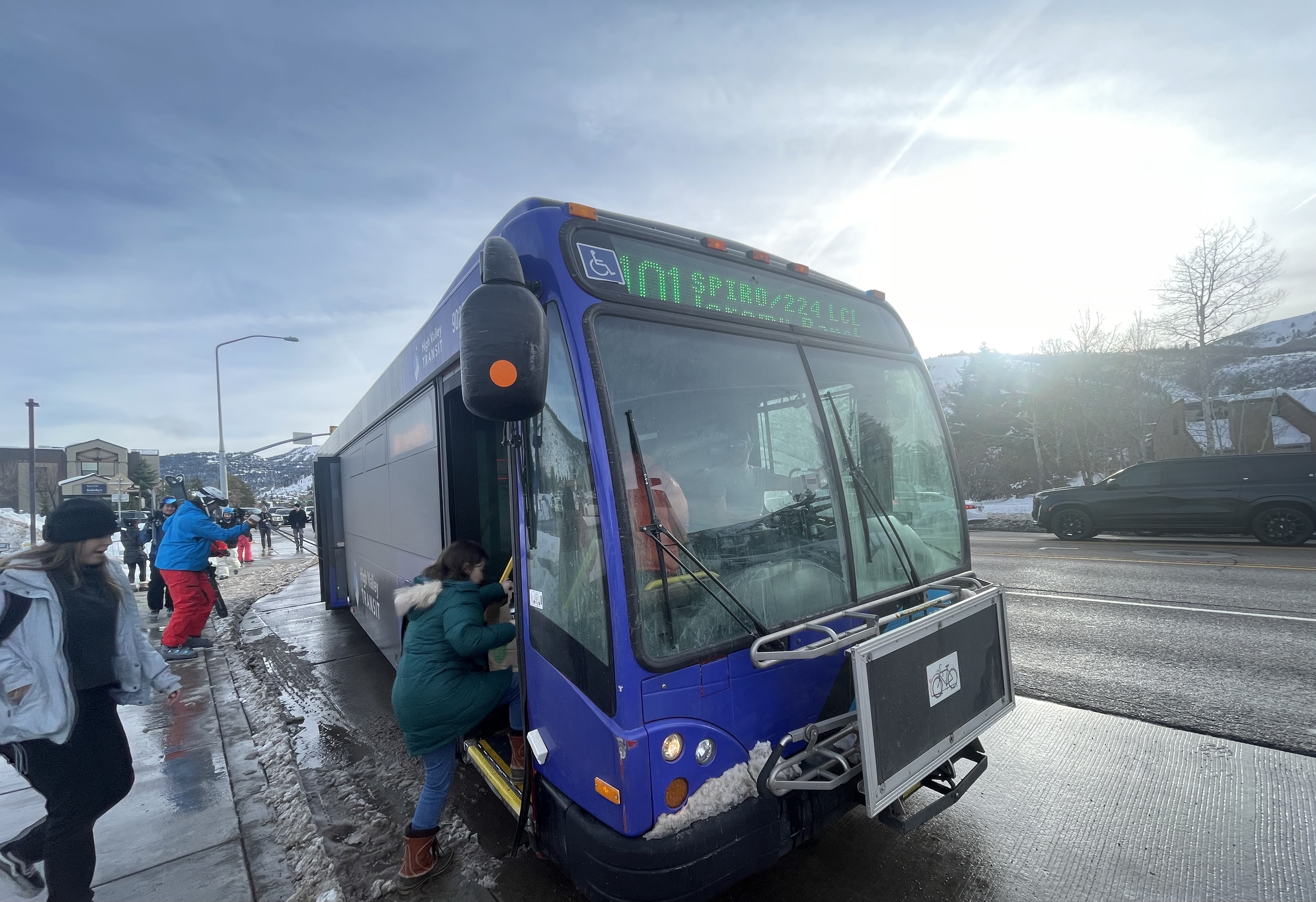 Blue articulated transit bus stopped at a snowy roadside stop, passengers boarding.
