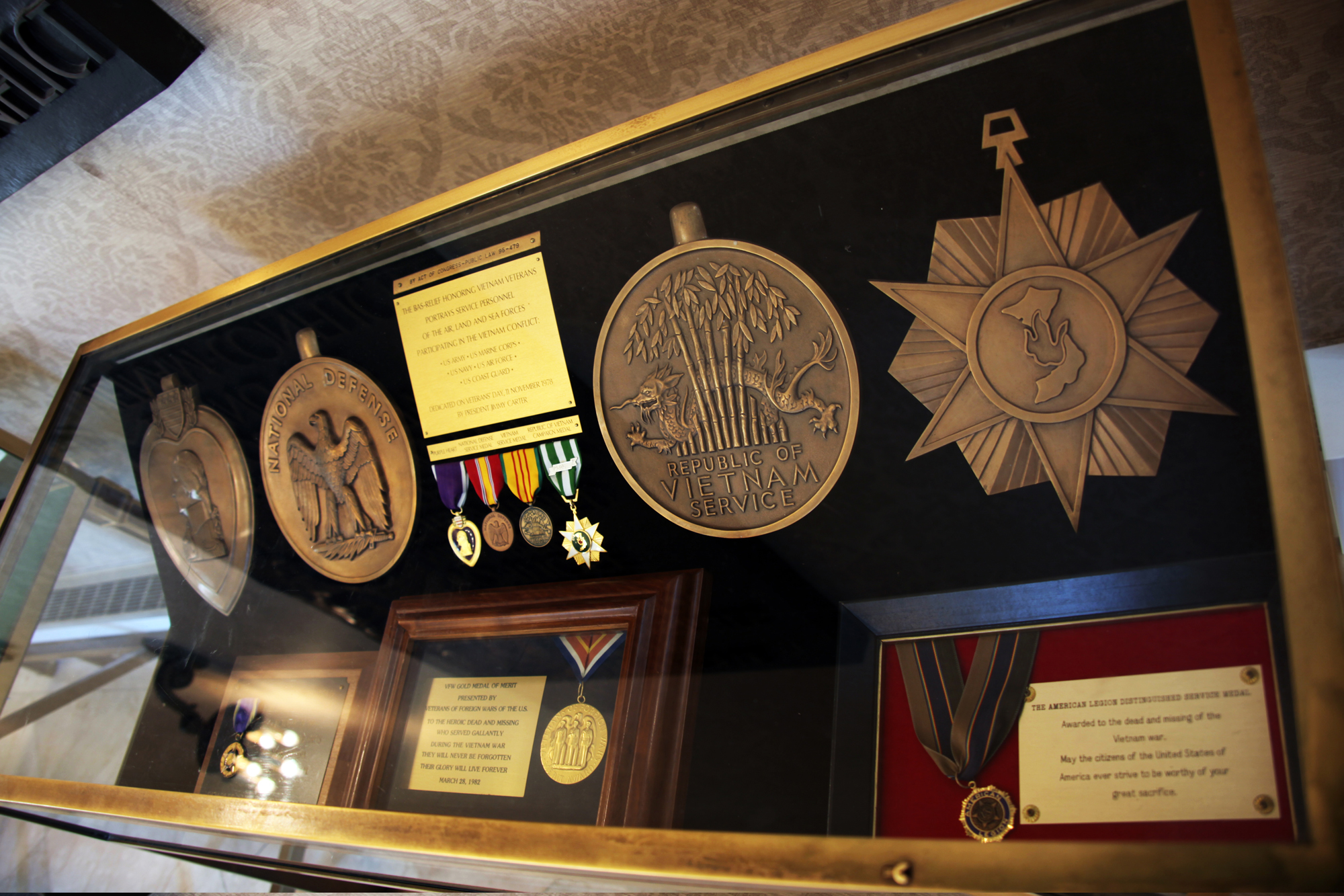 A glass display case holding Vietnam War military medals and decorations on a dark background.