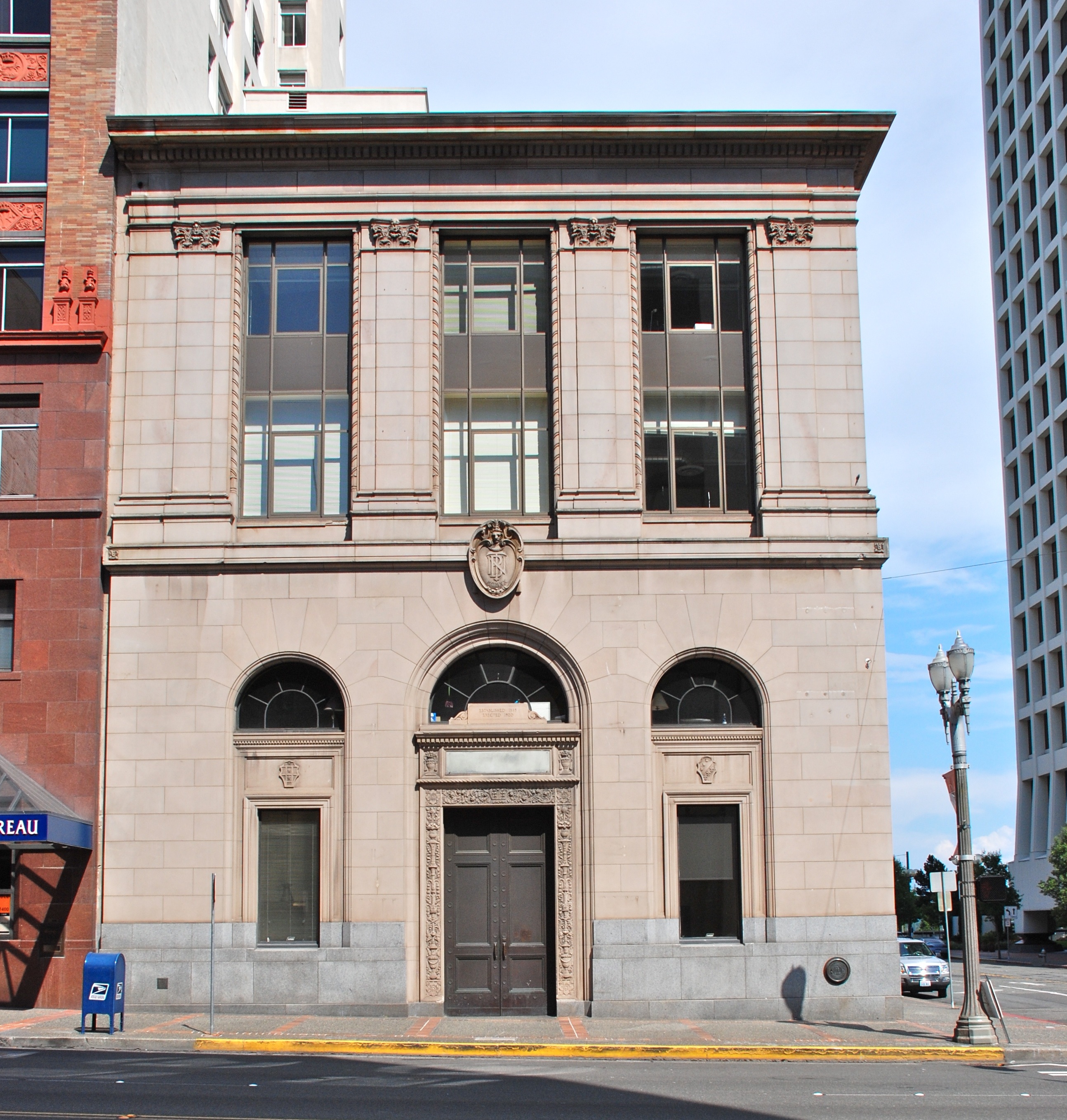 Neoclassical stone bank building facade with arched windows at a downtown Tacoma street corner.