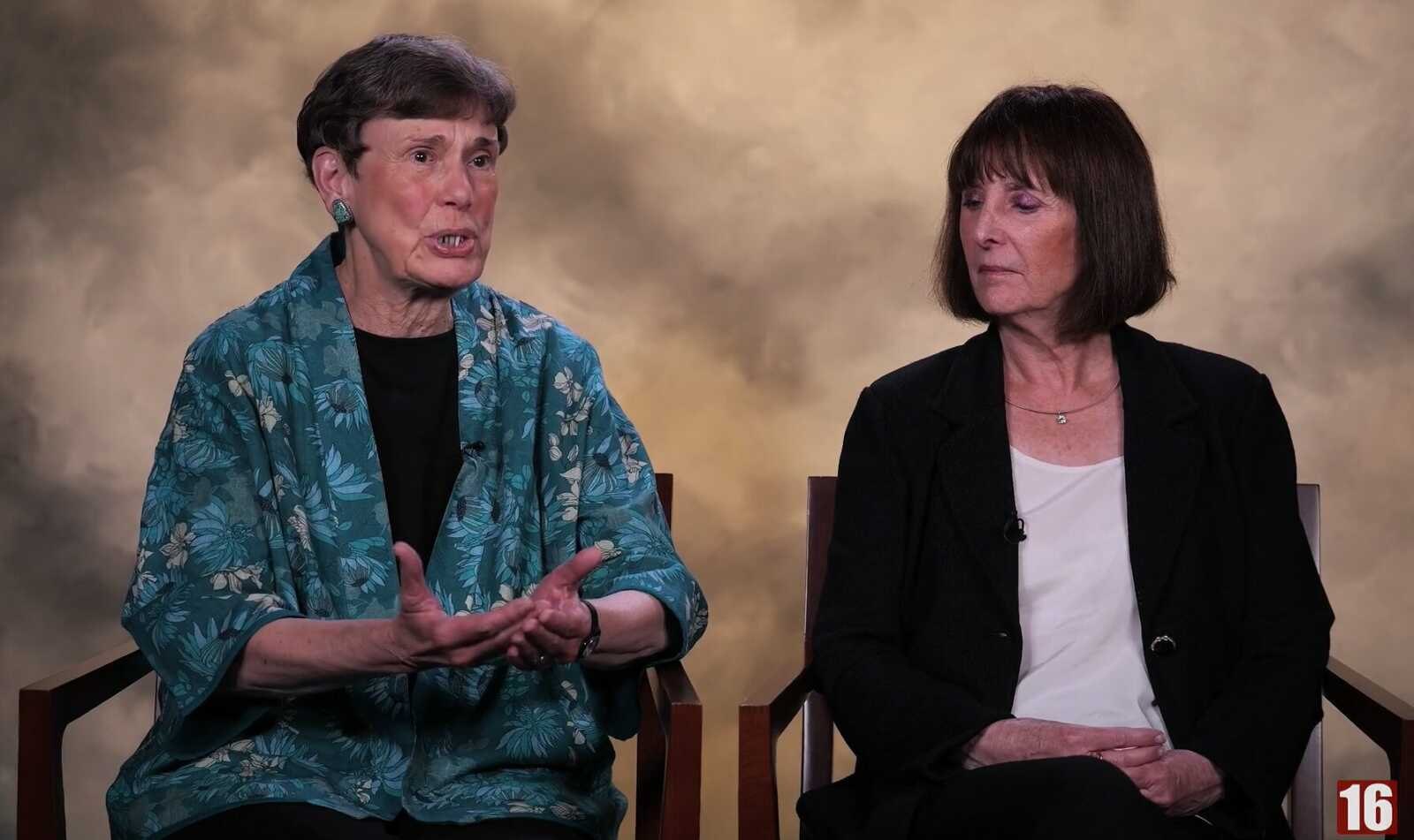 Two women seated in a studio interview setting, one gesturing while the other listens.