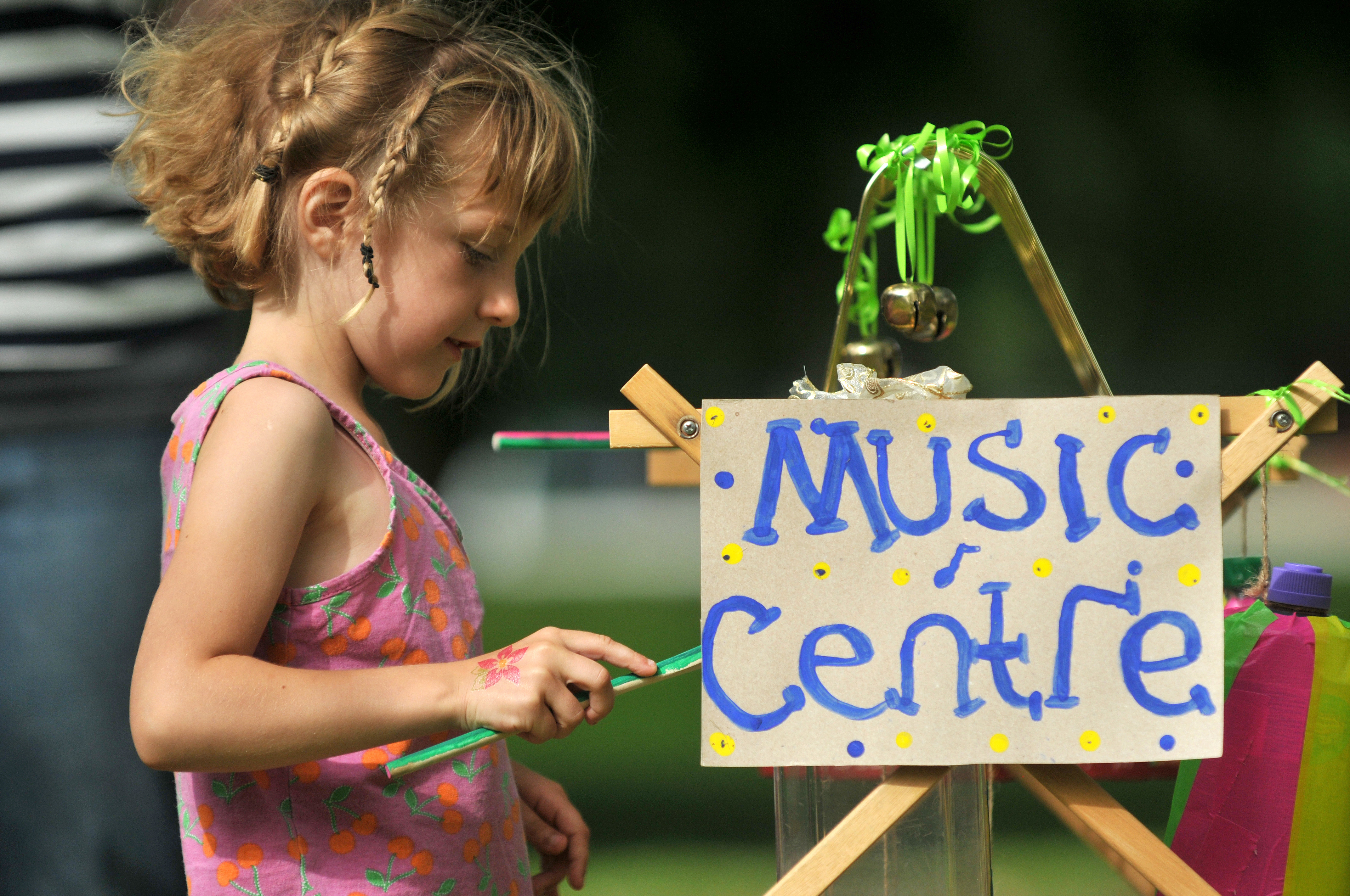 Young girl holding a green stick at an outdoor children's music activity station.