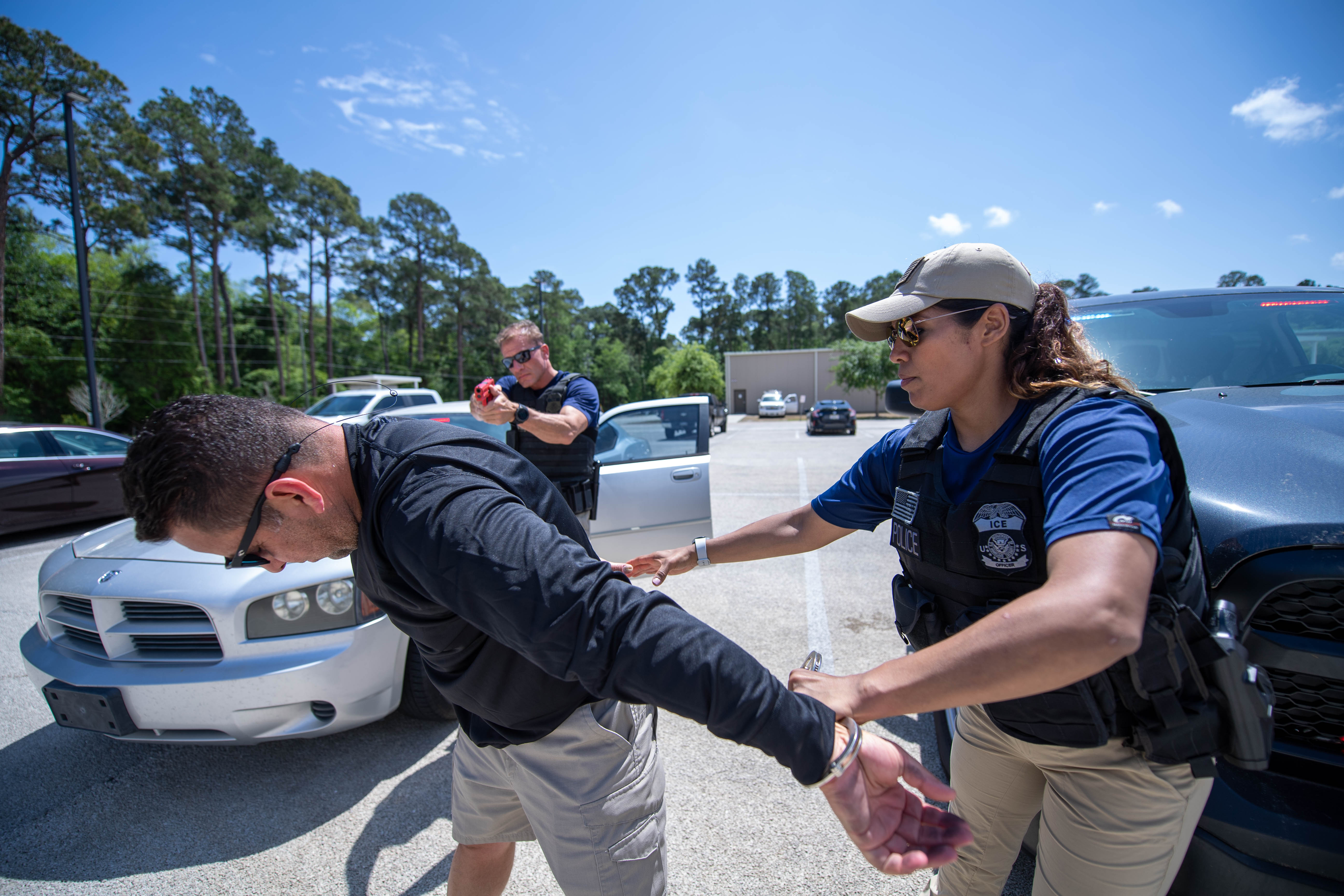 Two officers in blue tactical vests conduct a simulated arrest at a vehicle stop in a parking lot.