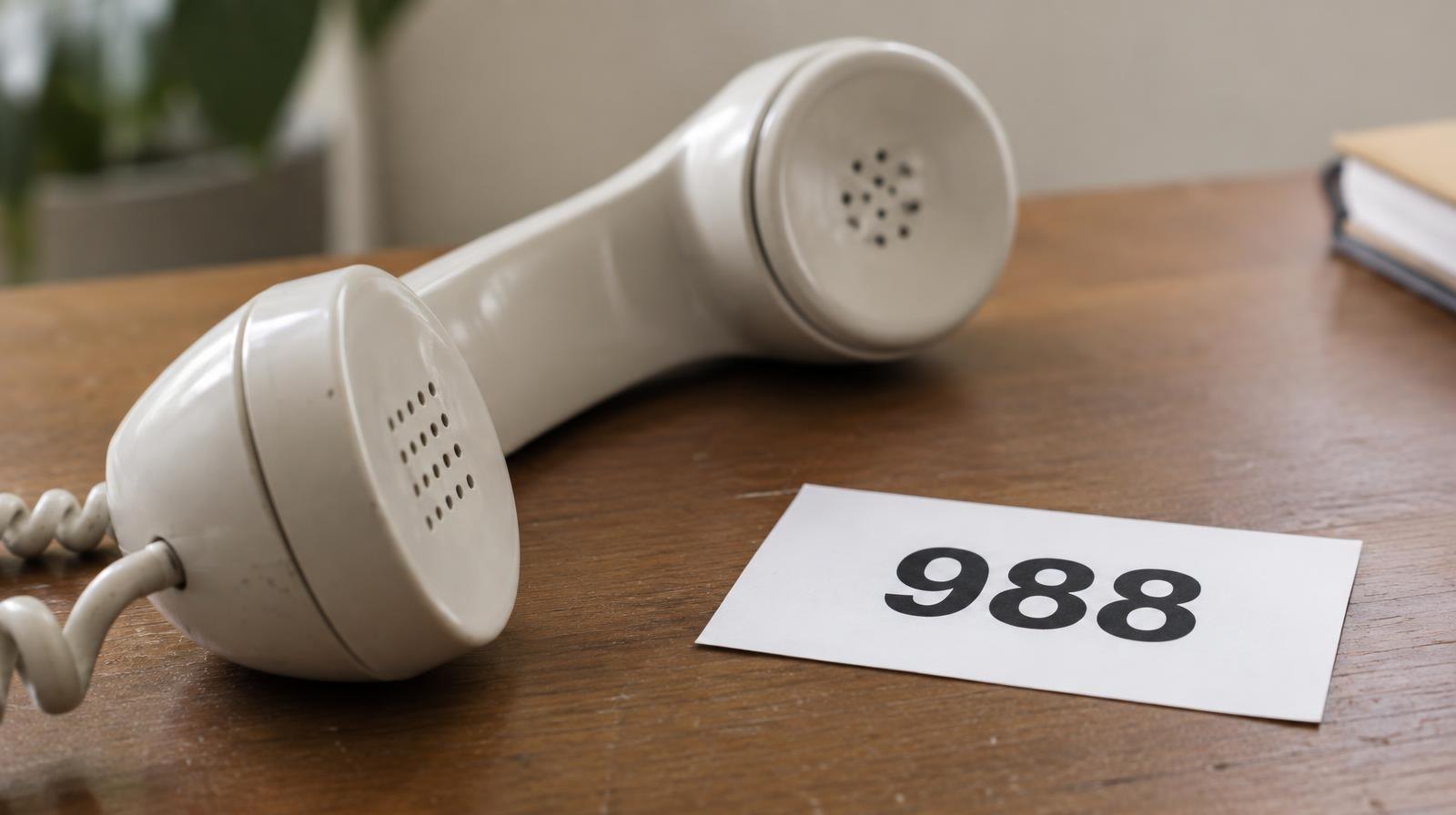 A telephone handset resting on a wooden surface beside a card with the number 988.