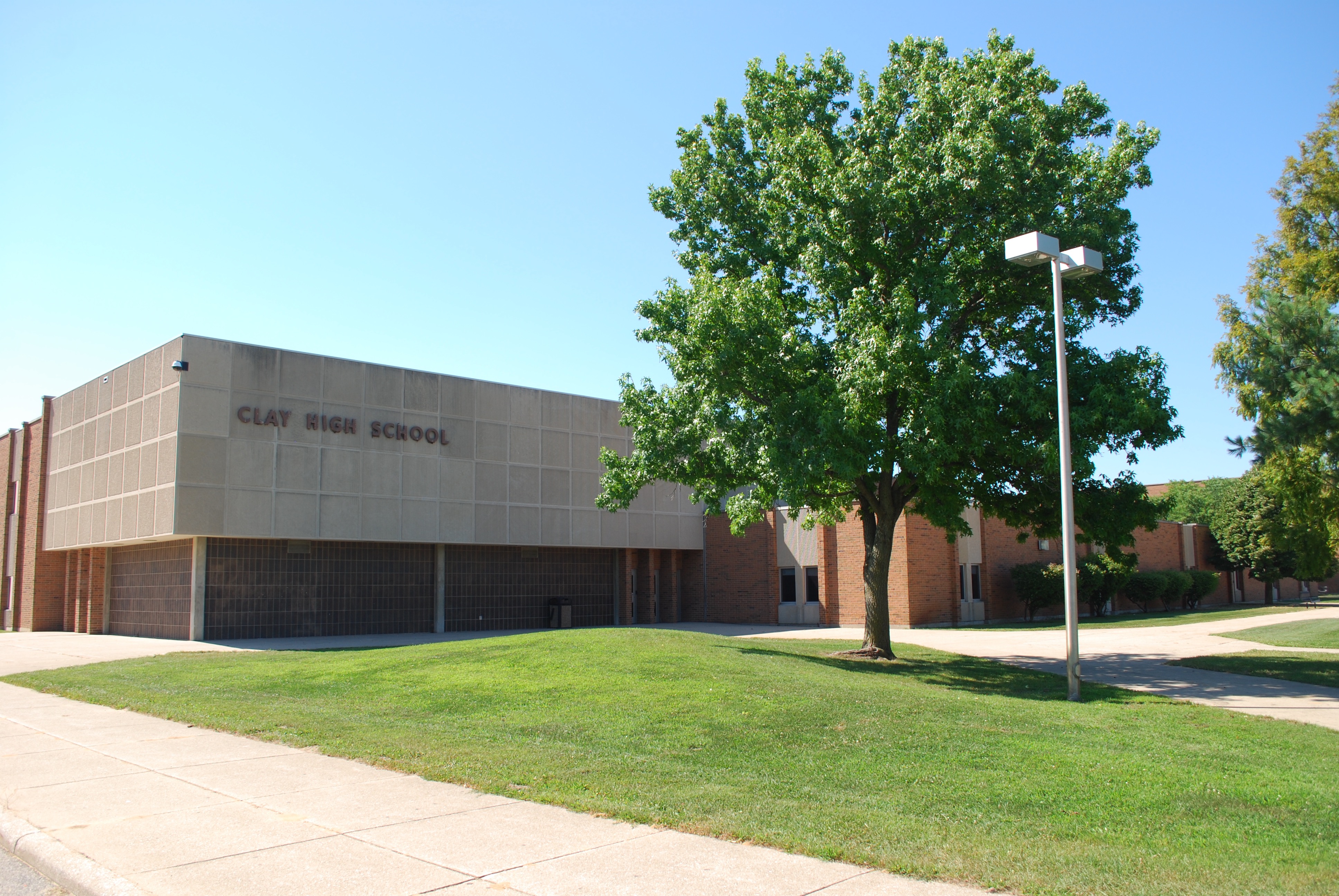Exterior of a school building with a sign reading Clay High School, green lawn, and a large tree.