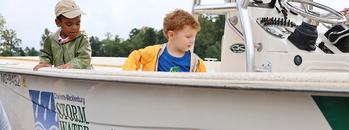 Two children leaning into a county water quality boat at an outdoor event.