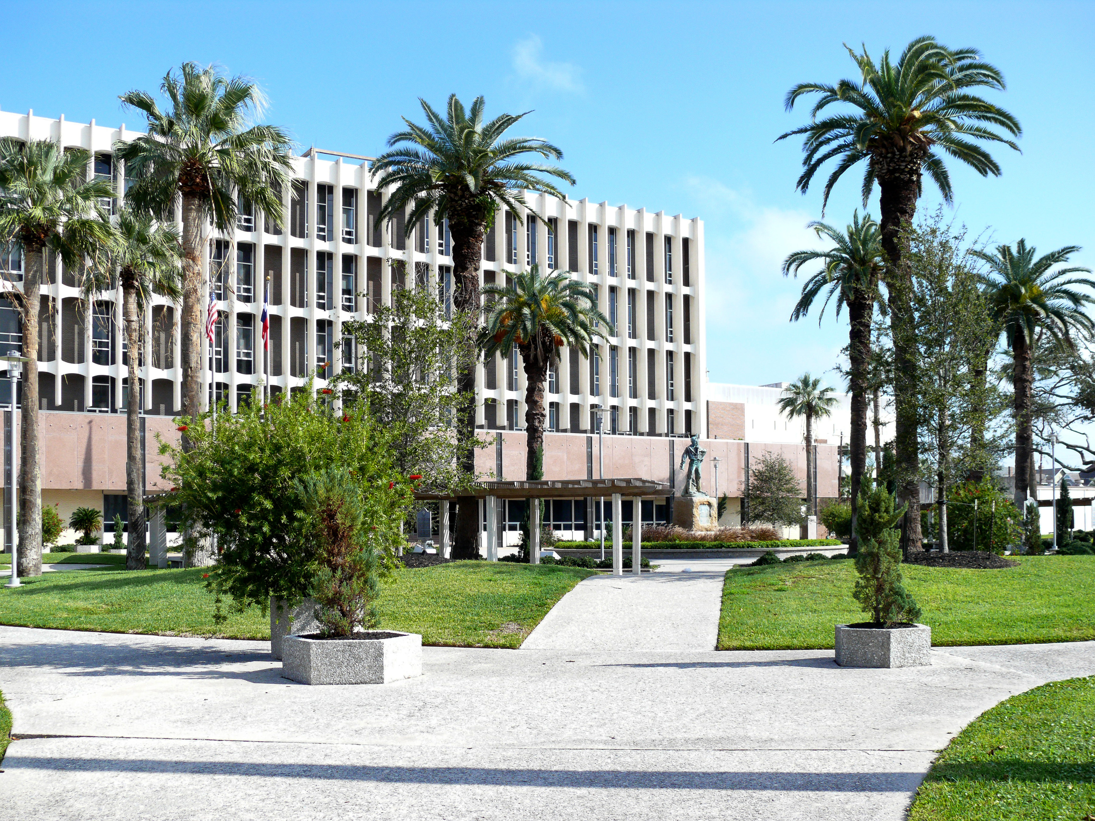 Multi-story government building with palm trees and a statue near the entrance.