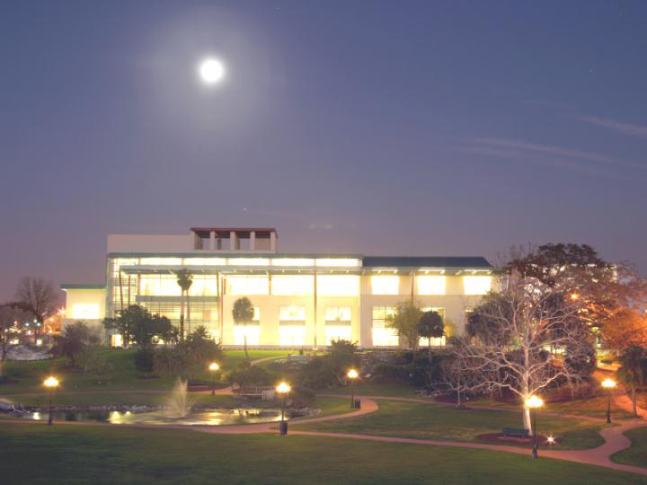 Large illuminated library building at night with a full moon and a fountain in the foreground.