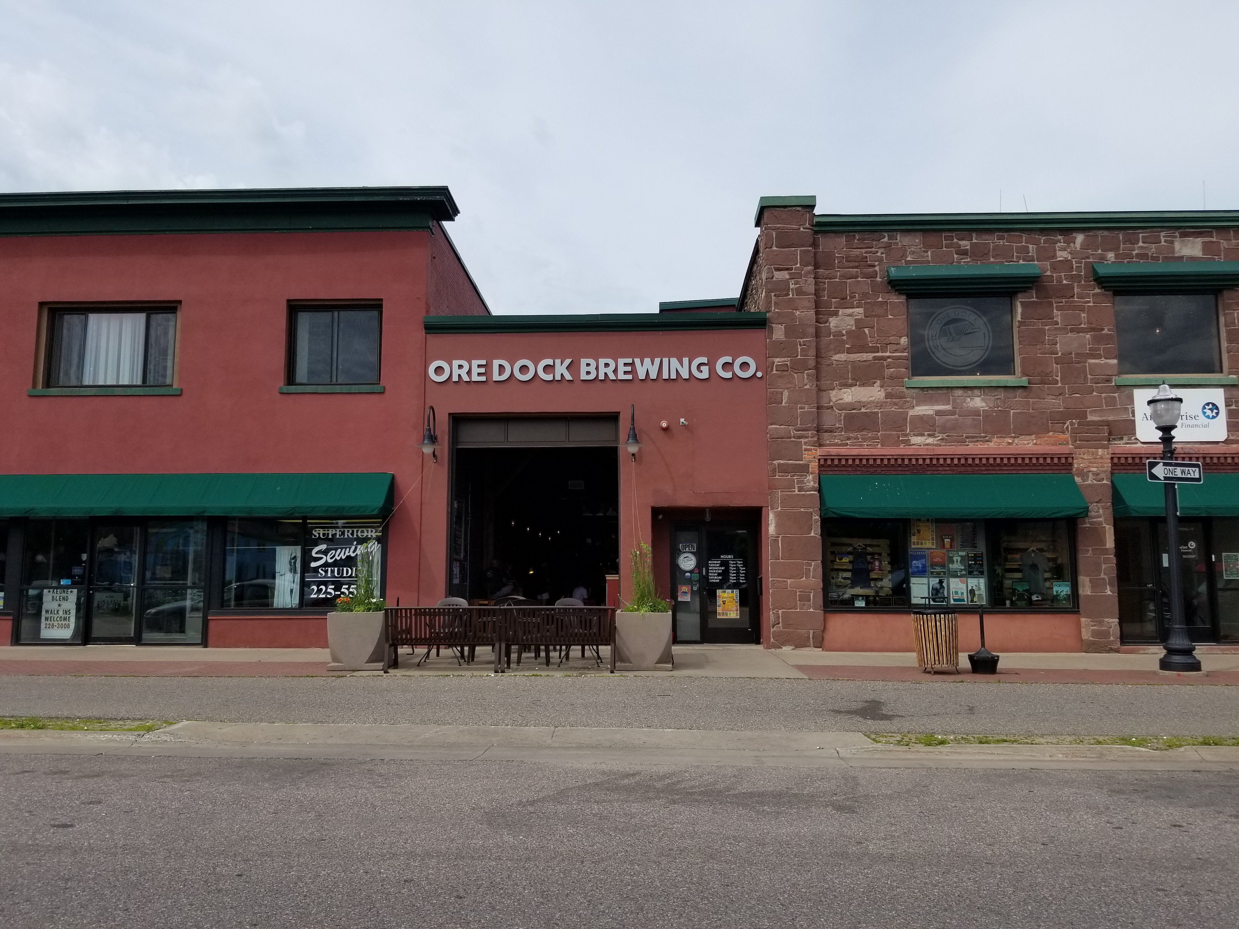 Red brick brewery exterior with green awnings and outdoor seating area.