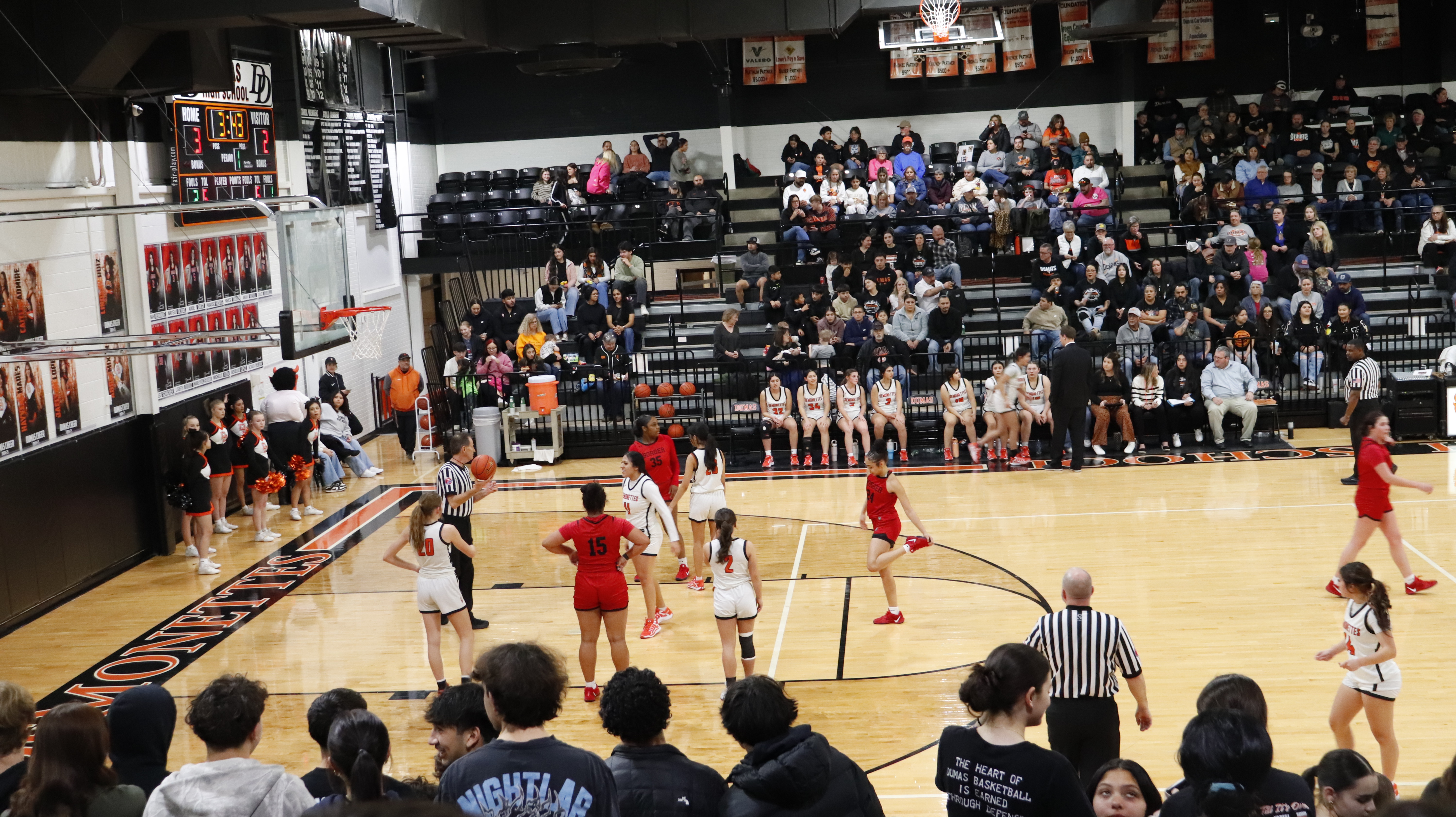 Girls basketball players on a gymnasium court with spectators in the stands.