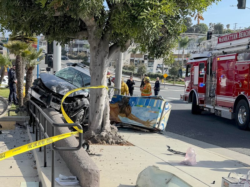 Crashed SUV on sidewalk with toppled signal box, fire truck, and yellow caution tape at crash scene.
