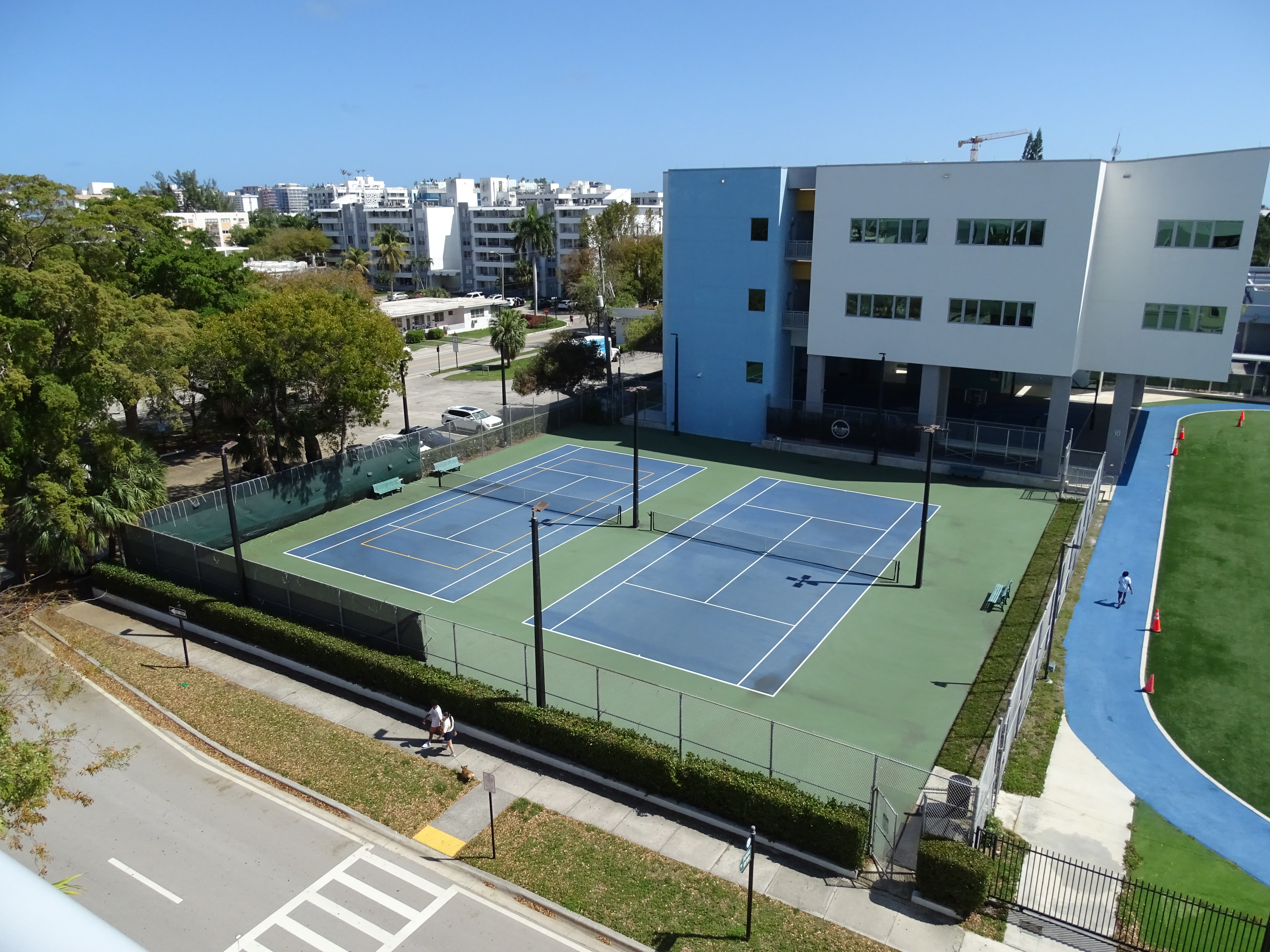 Aerial view of a school campus with two blue tennis courts and a multi-story building.
