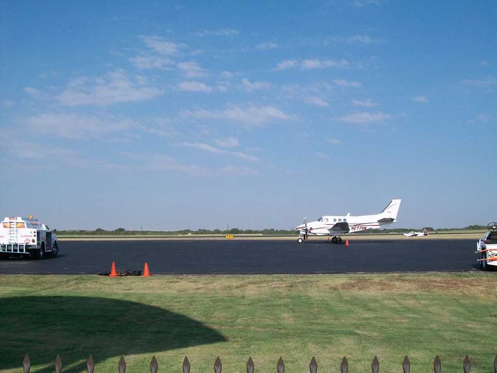 Twin-engine propeller plane parked on tarmac at a small Texas airport.
