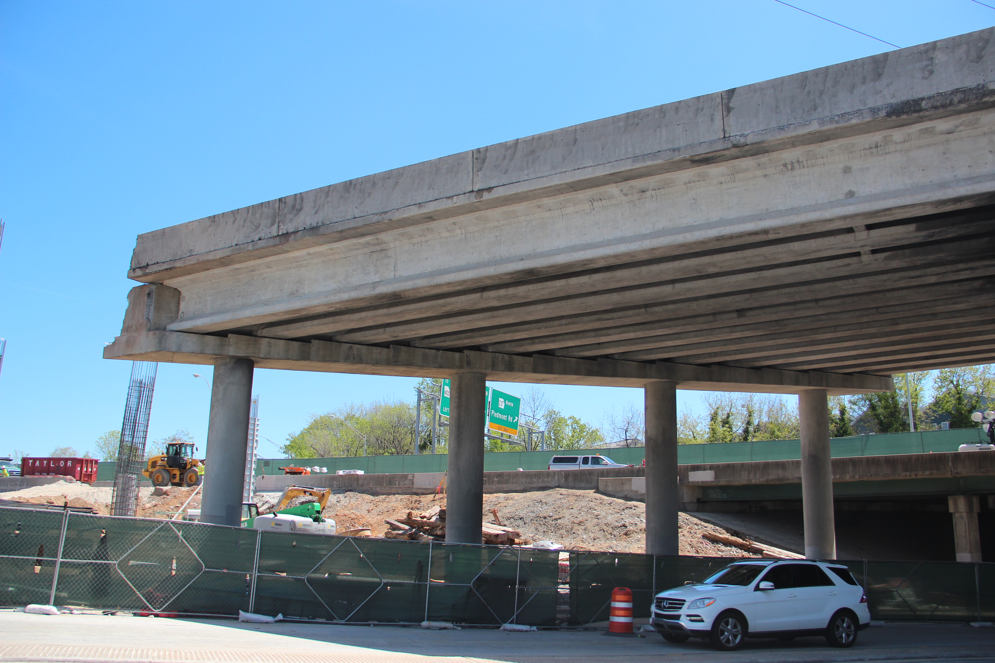 Collapsed concrete highway overpass with support columns, surrounded by green construction fencing.