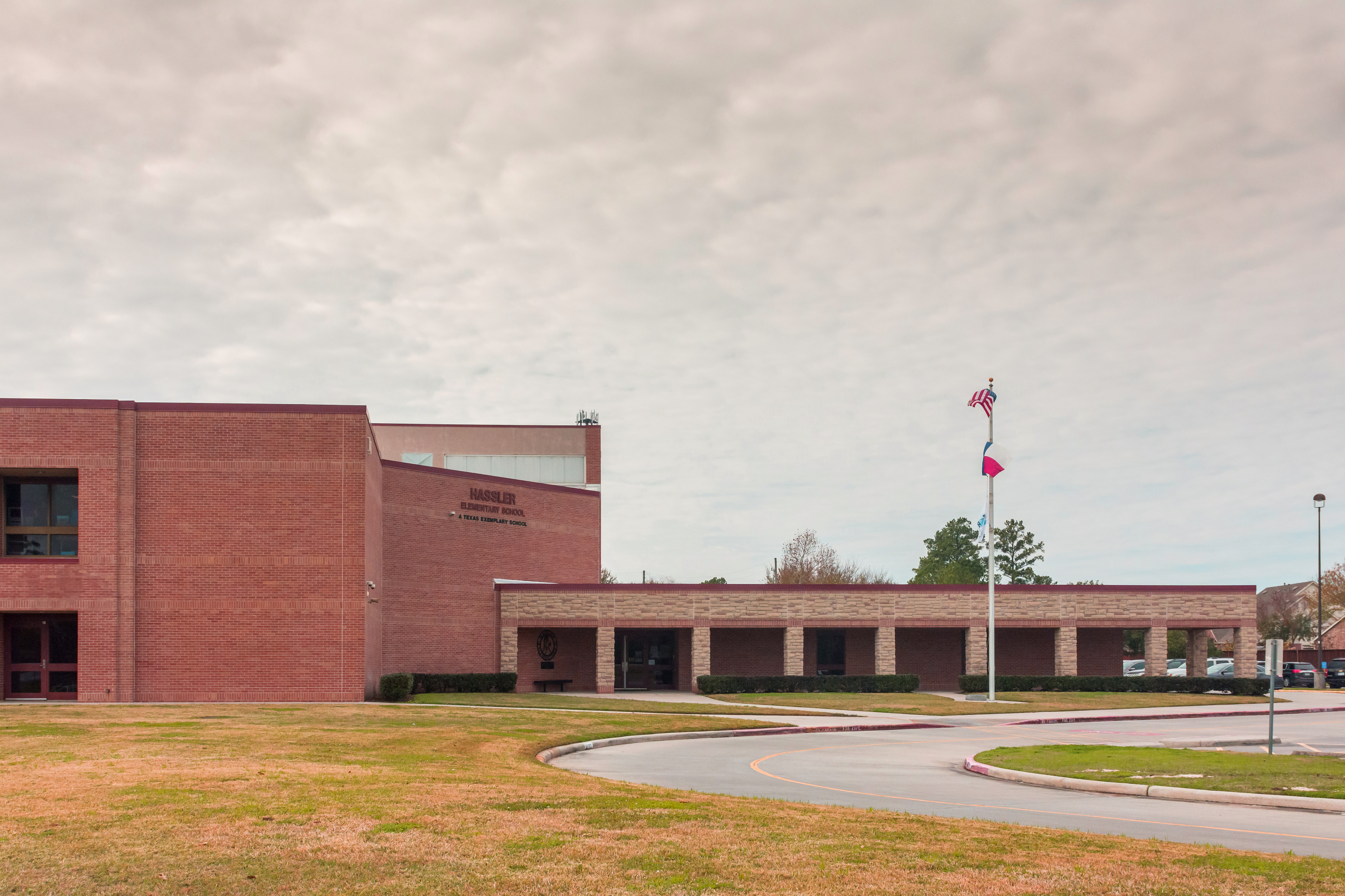 Red brick school building with flagpole and circular driveway under overcast sky.
