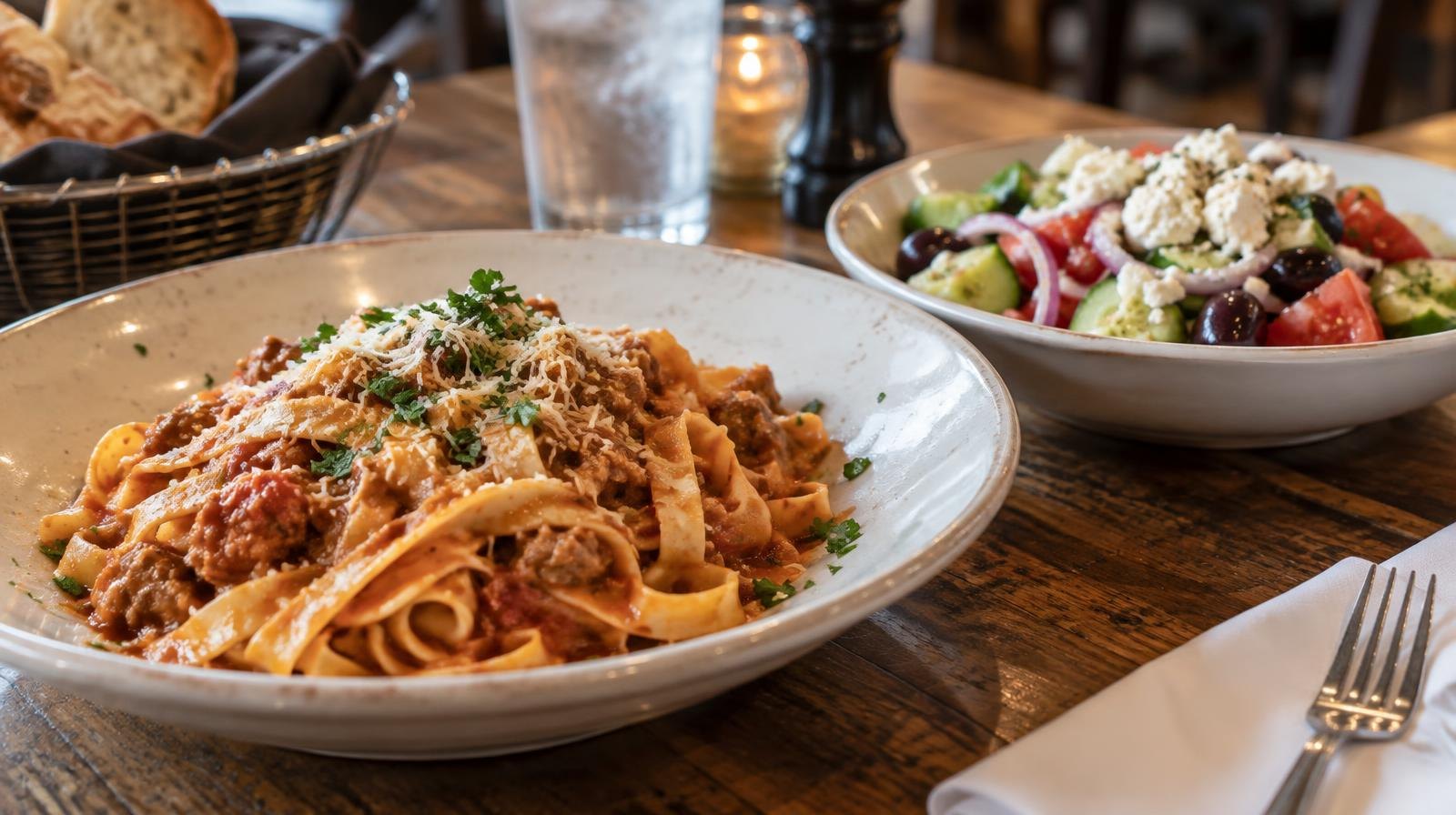 Plate of homemade pasta and Greek salad on a wooden restaurant table.