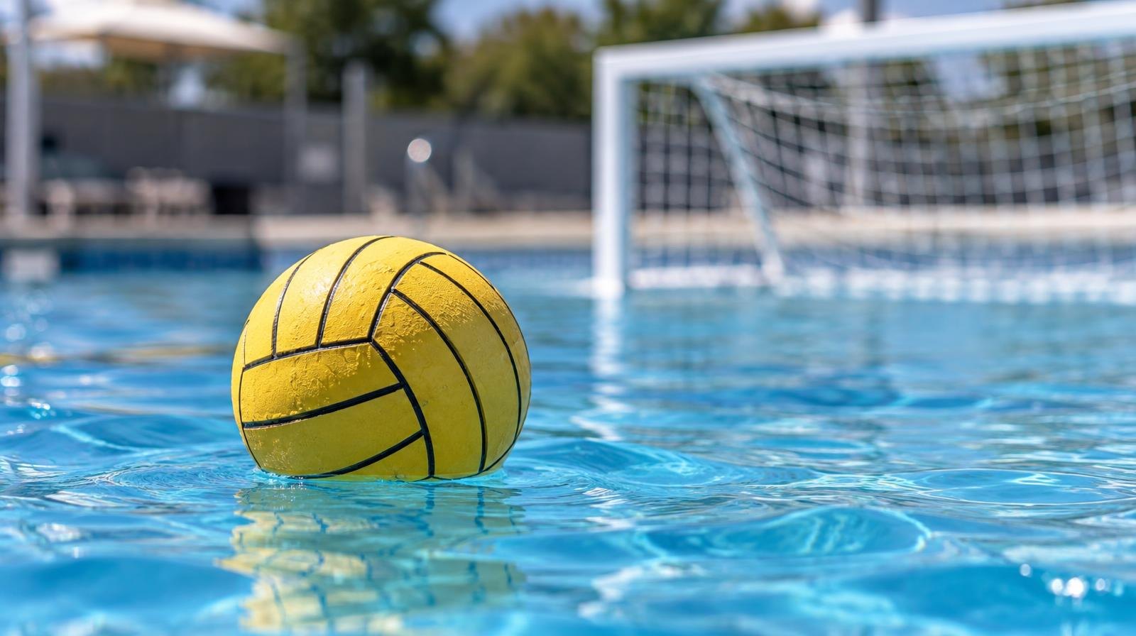 A water polo ball floating on a bright blue pool surface near a goal net.