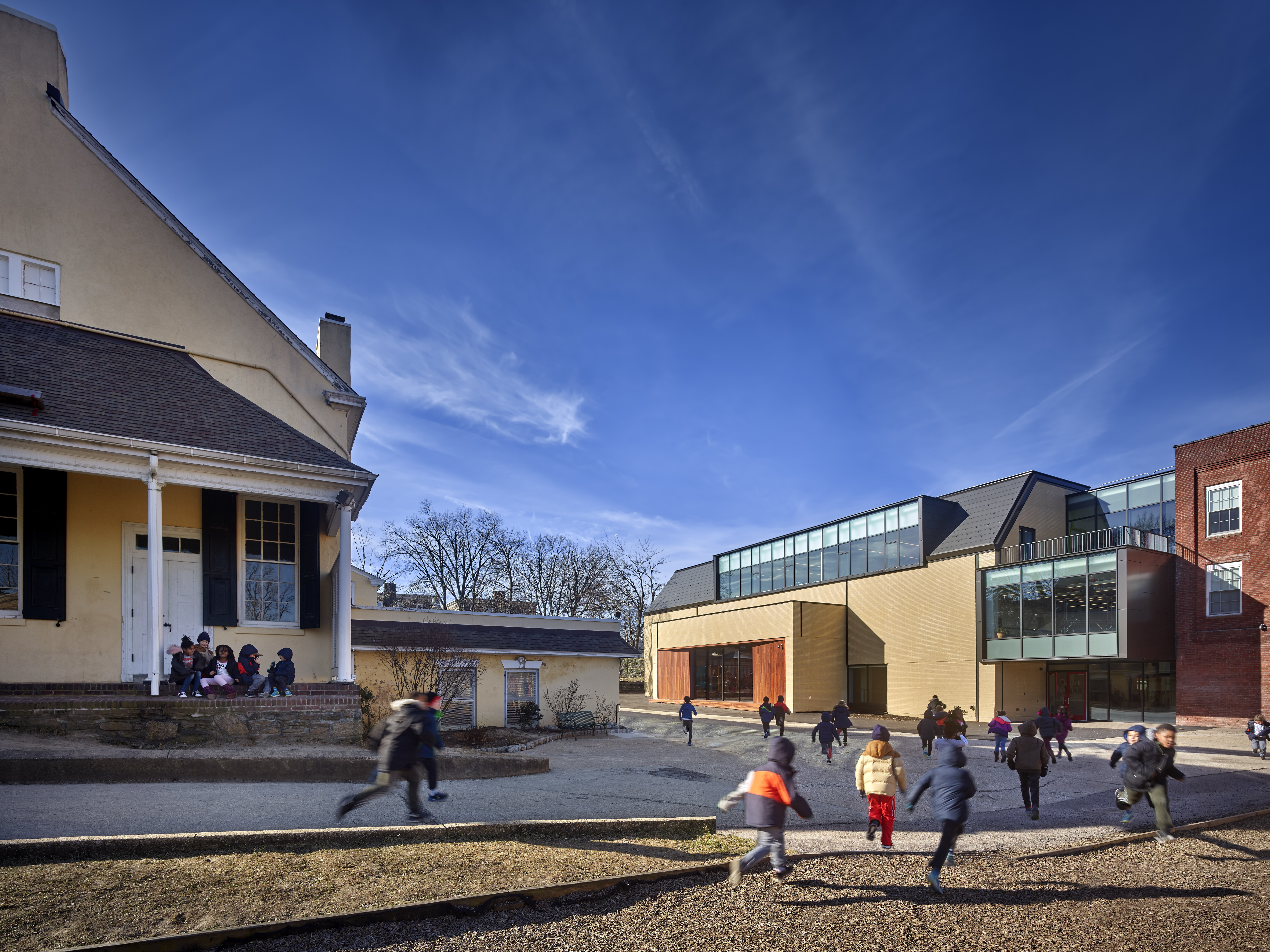 Children running and playing in an outdoor school courtyard on a sunny day.