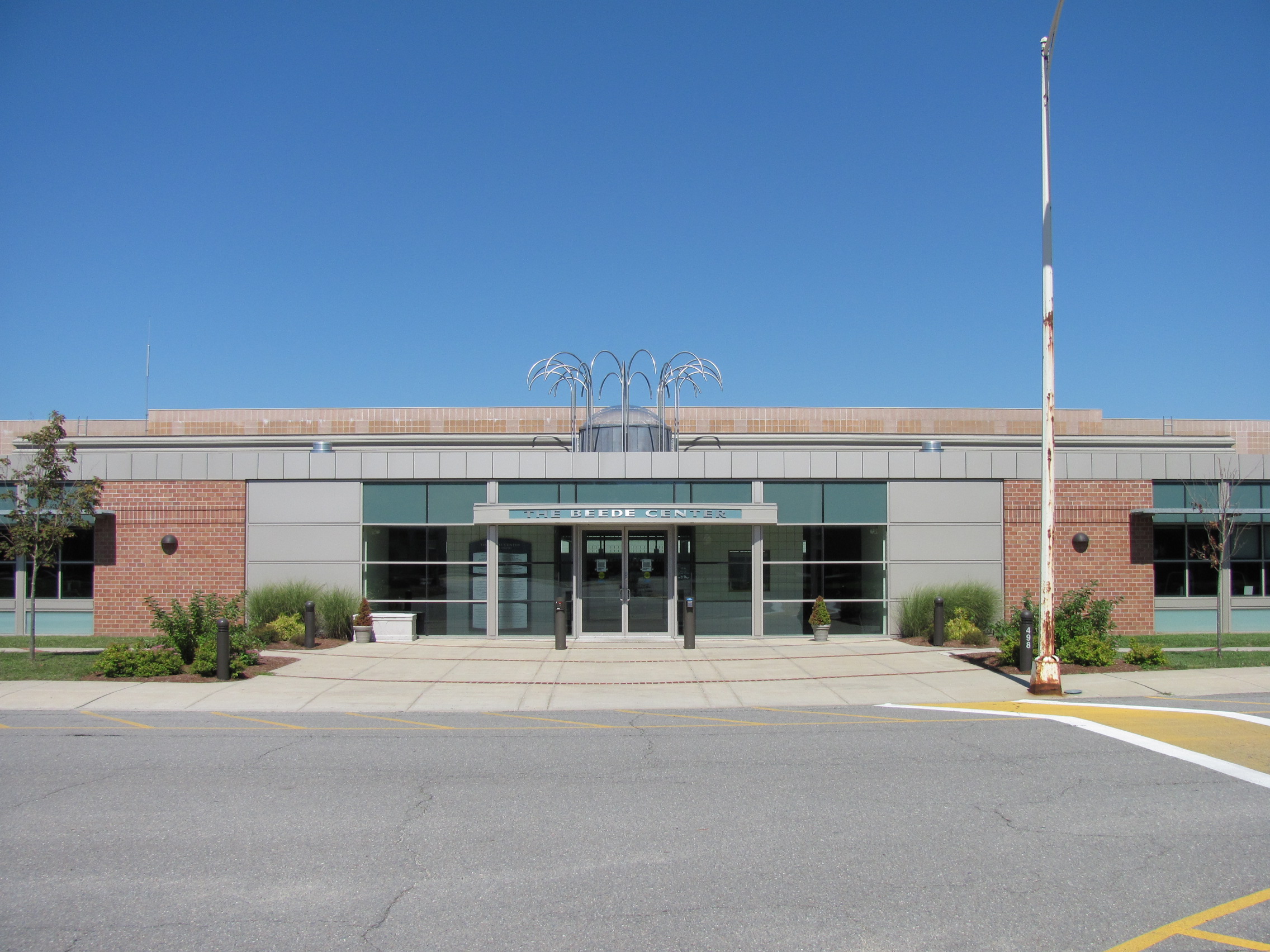 Brick and glass school building entrance with flagpole and decorative metalwork above the door.
