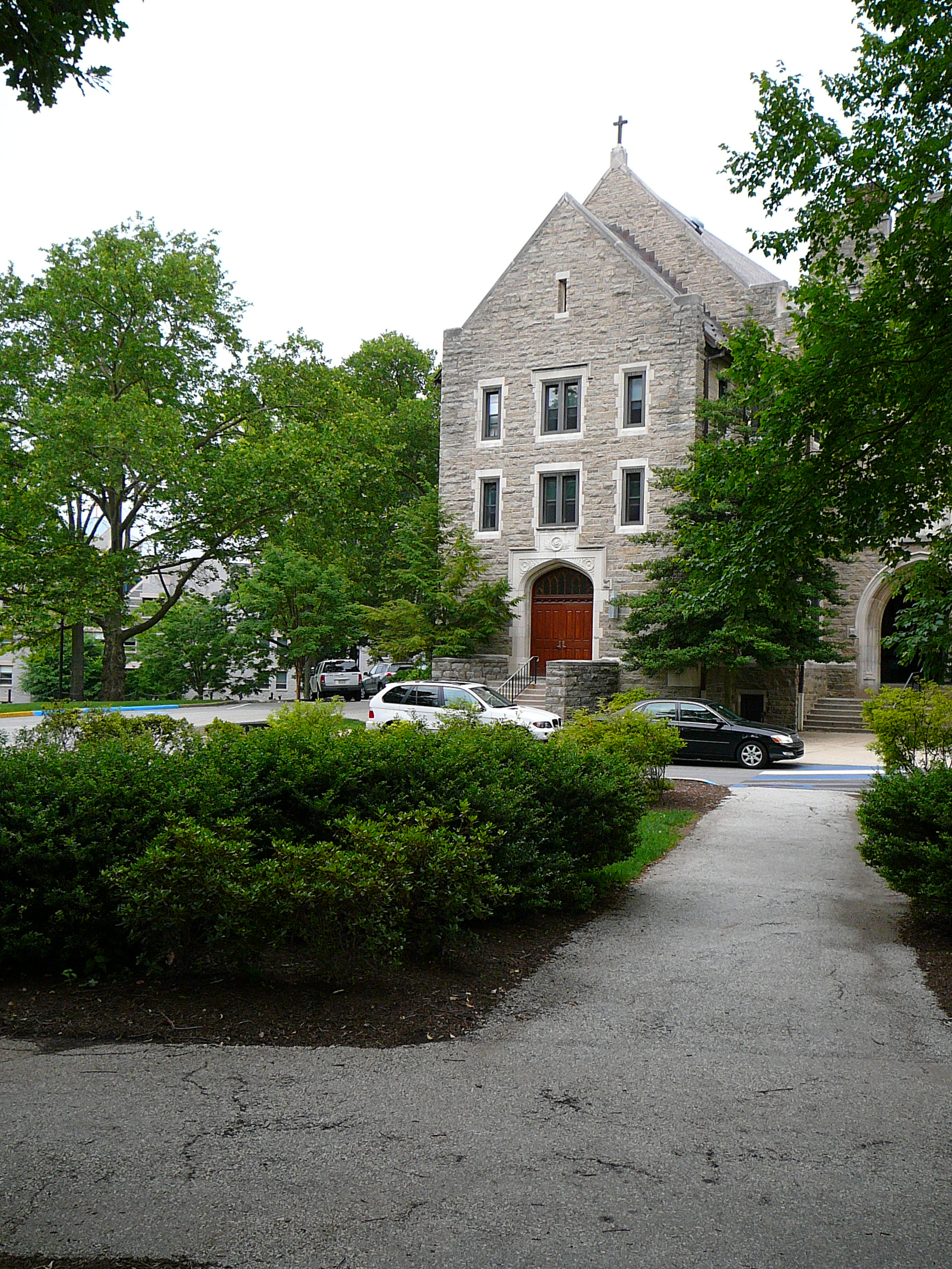 Gothic stone university building with arched entrance surrounded by trees.