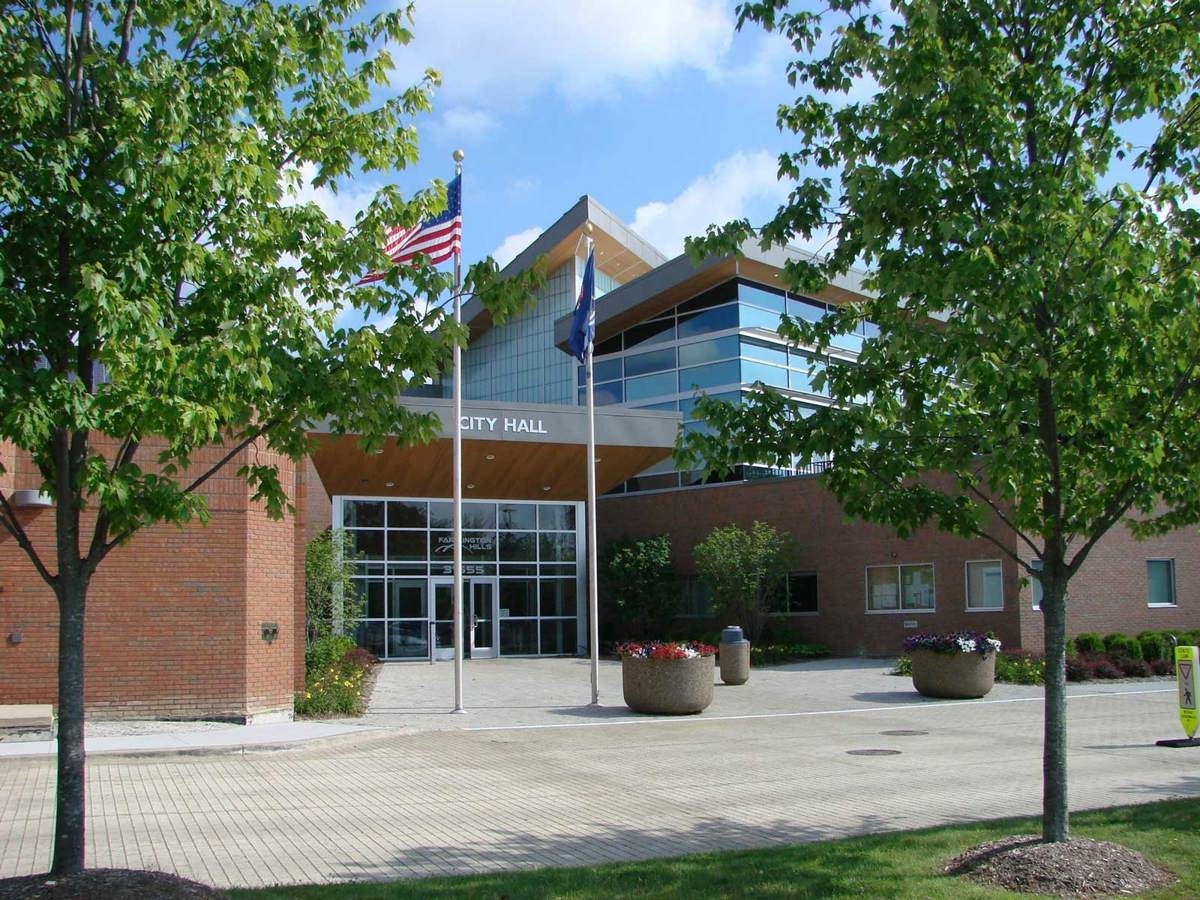 Brick municipal building labeled City Hall with an American flag on a flagpole in front.