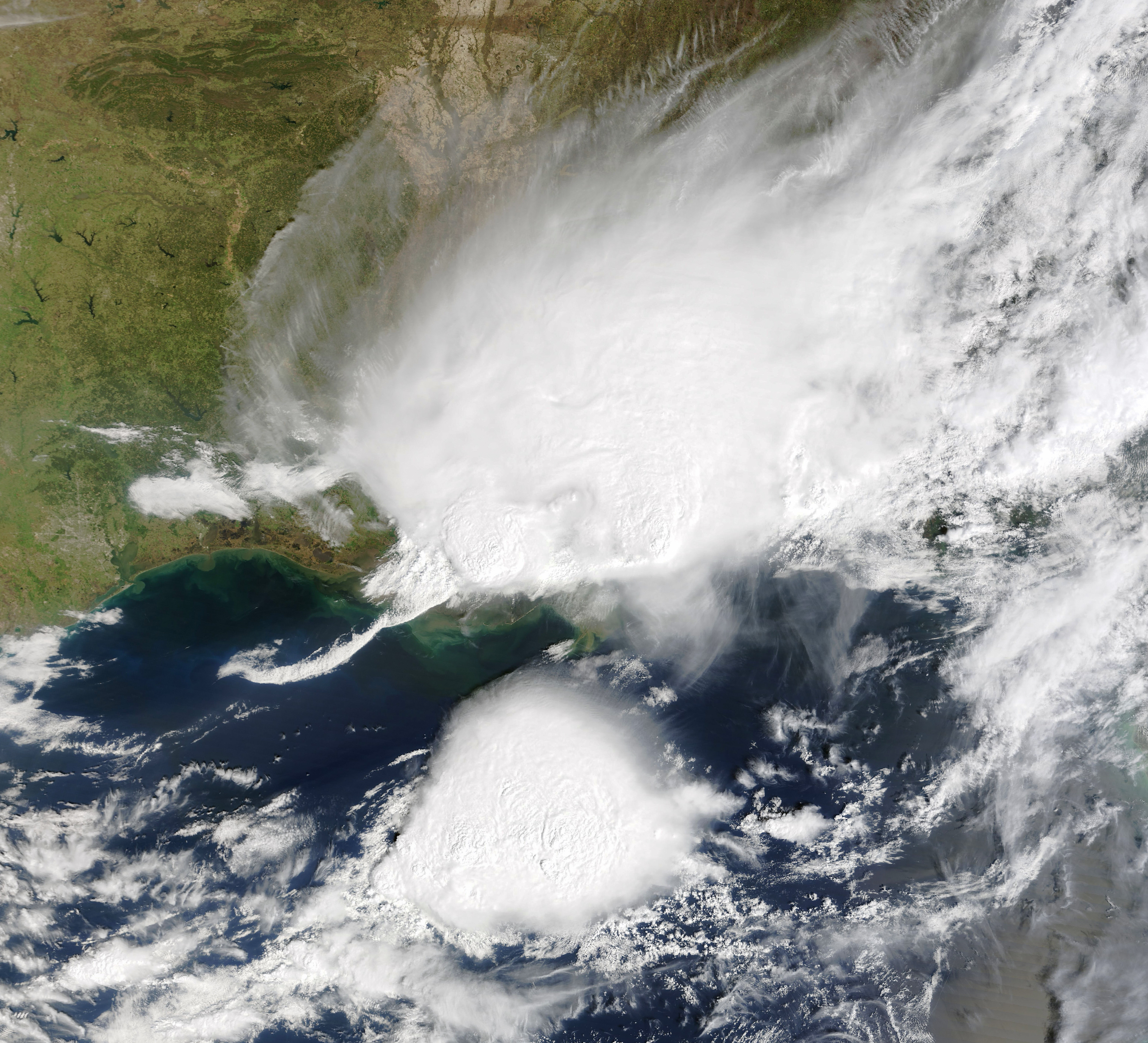 Satellite view of a large storm system with towering anvil clouds over land.