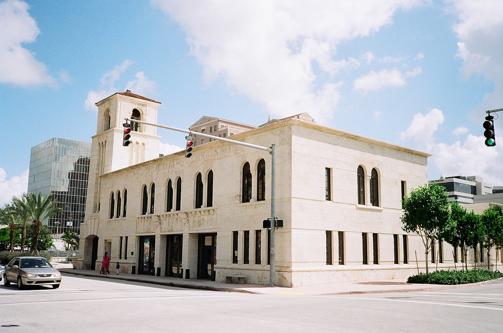 Historic limestone building with arched windows and a corner bell tower on a sunny street corner.