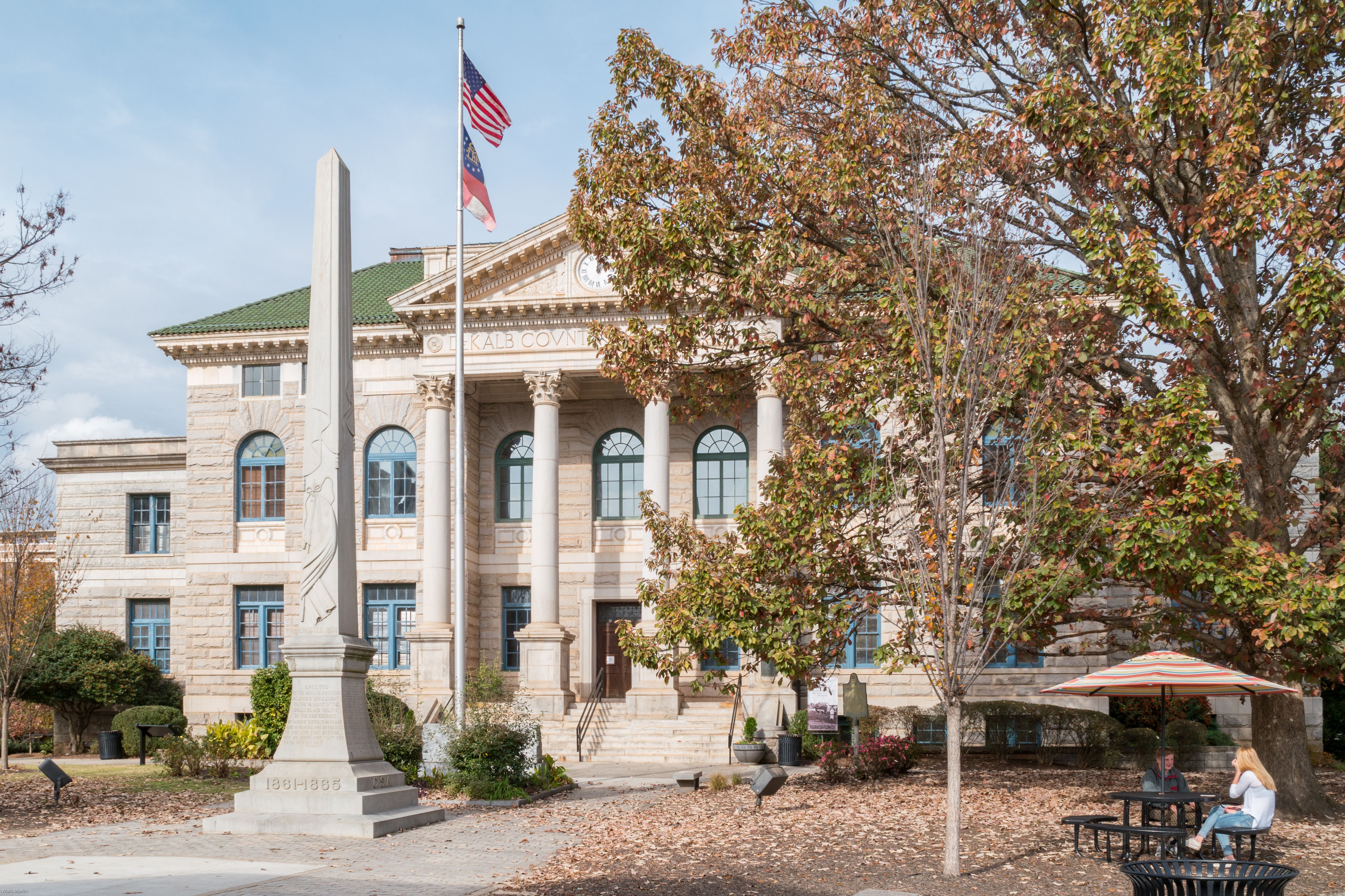 Neoclassical stone courthouse with columns, flags, and an obelisk monument in the foreground plaza.