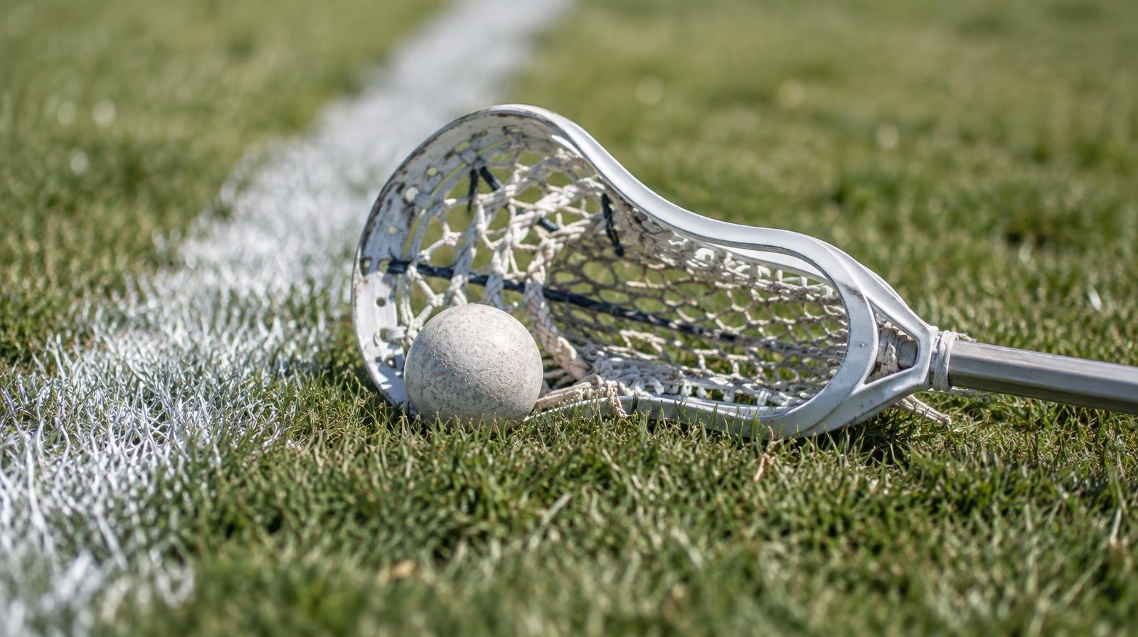 A lacrosse stick and ball resting on green grass beside a white boundary line.