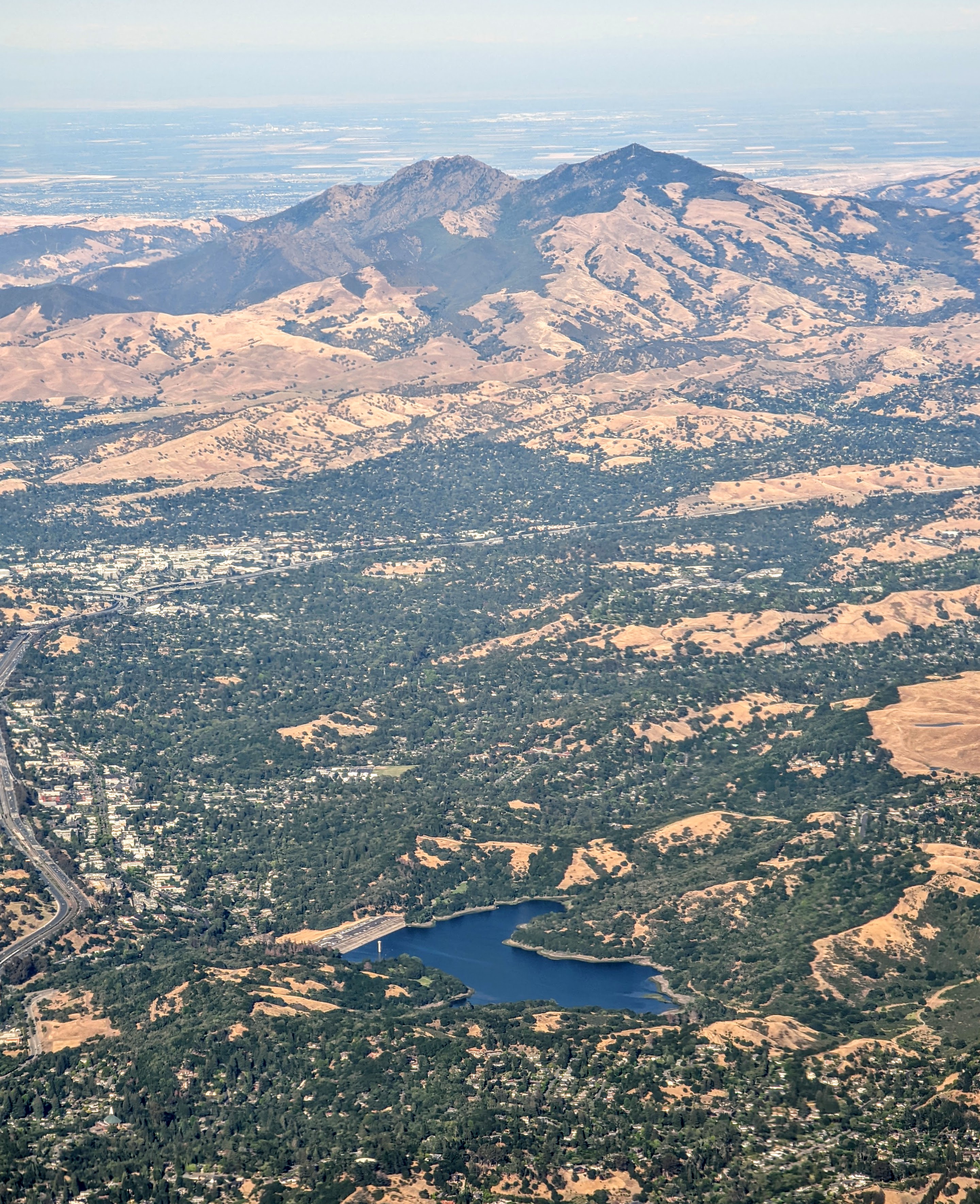 Aerial view of a blue reservoir surrounded by tree-lined suburban neighborhoods and golden hills.
