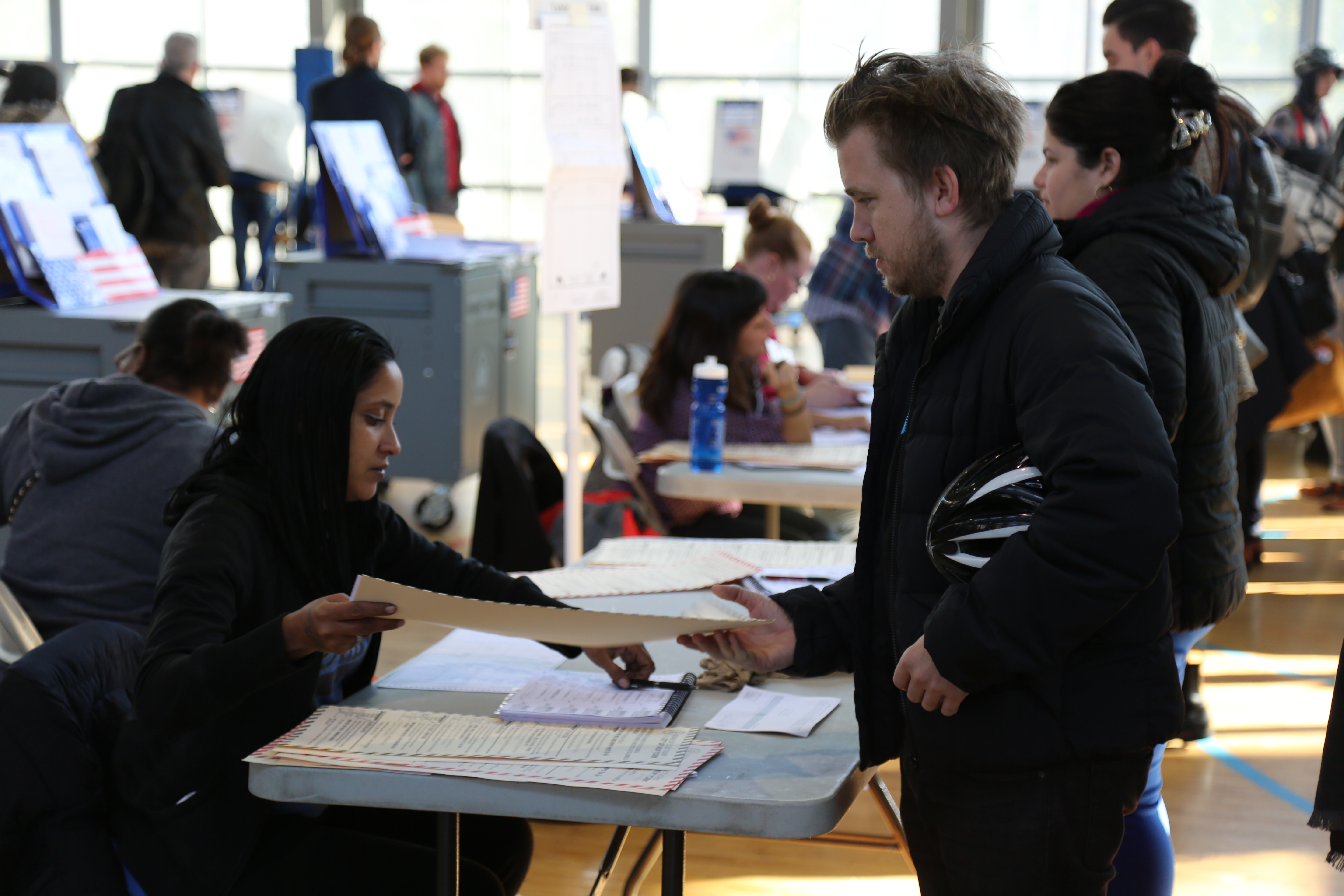 An election worker hands a ballot to a voter at a polling station with booths in the background.