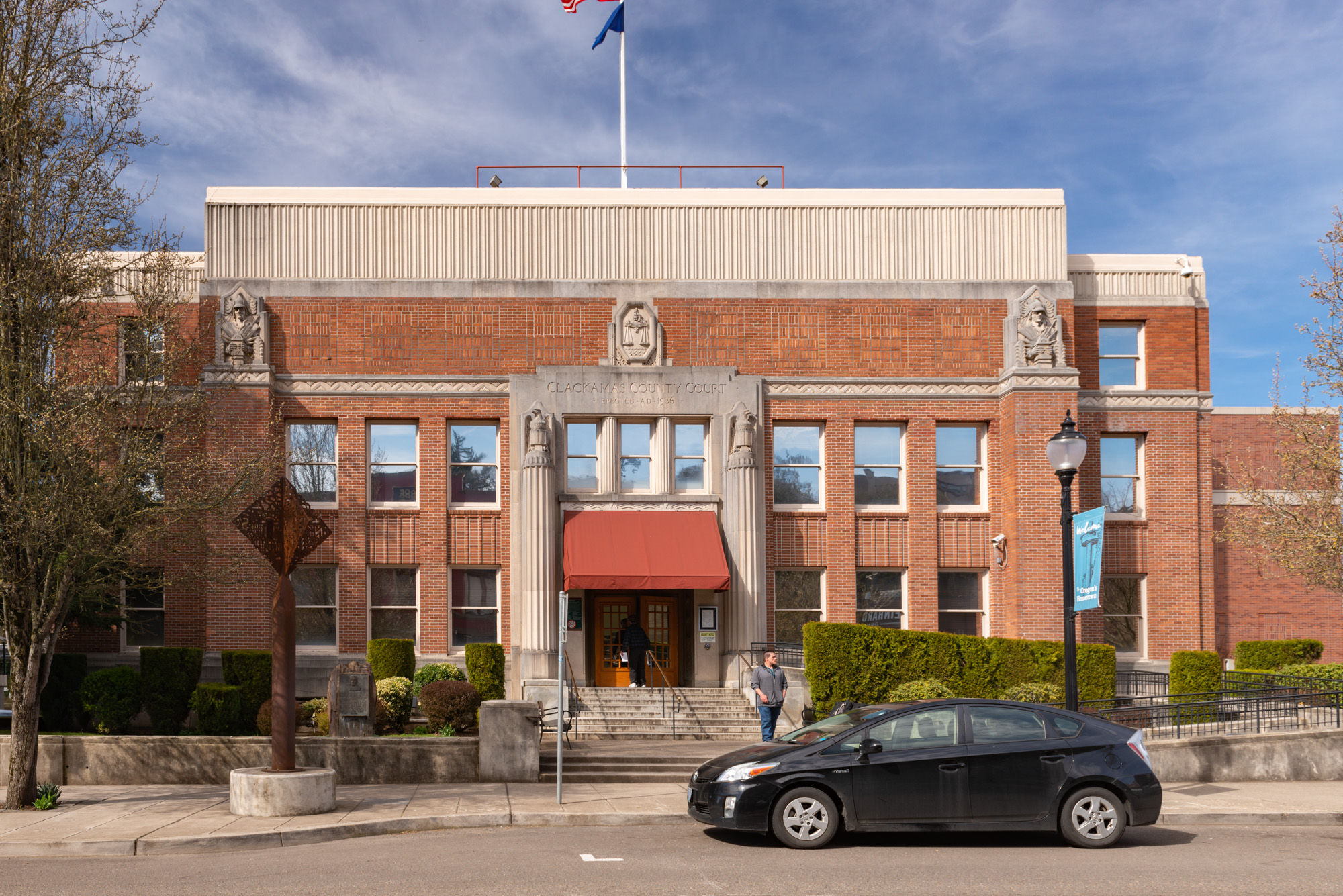 Two-story red-brick government building with classical columns and American flag.