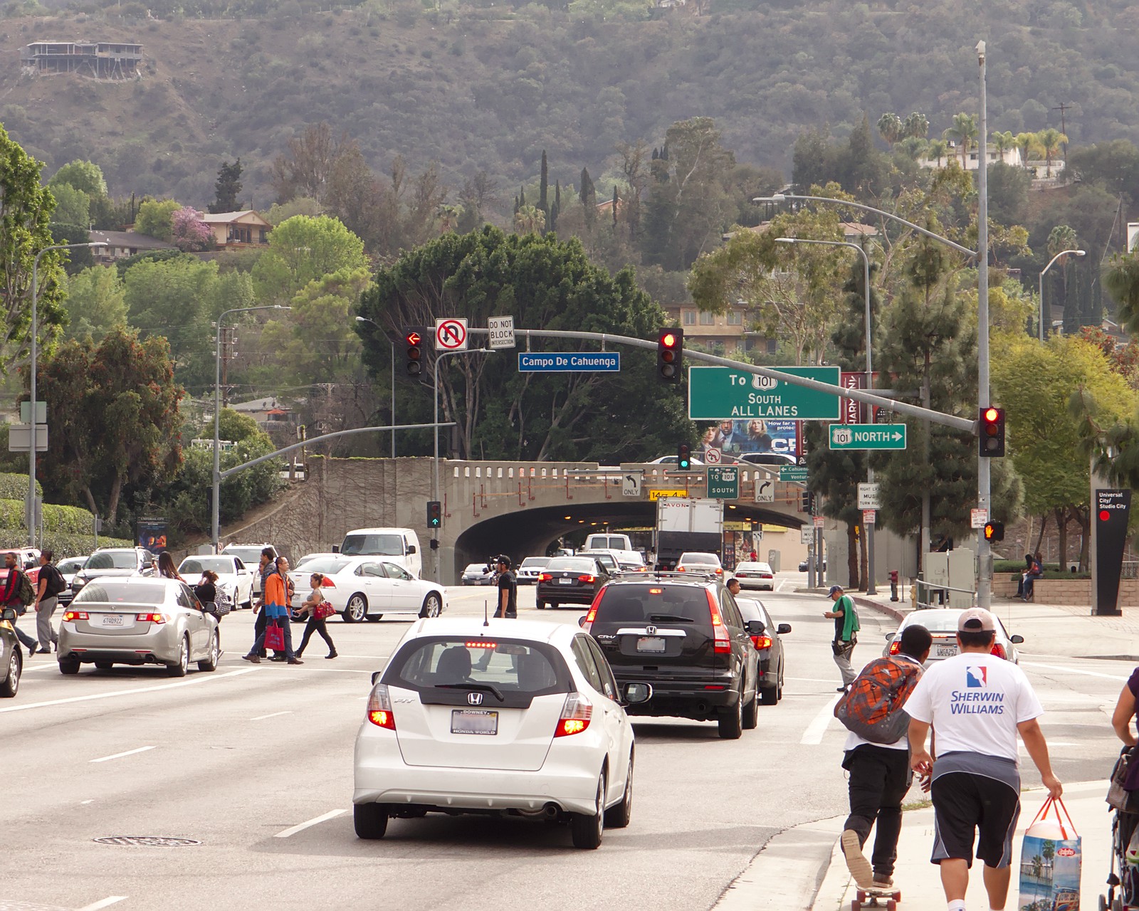 Busy multi-lane boulevard with cars, traffic signals, and freeway signs in an urban neighborhood.