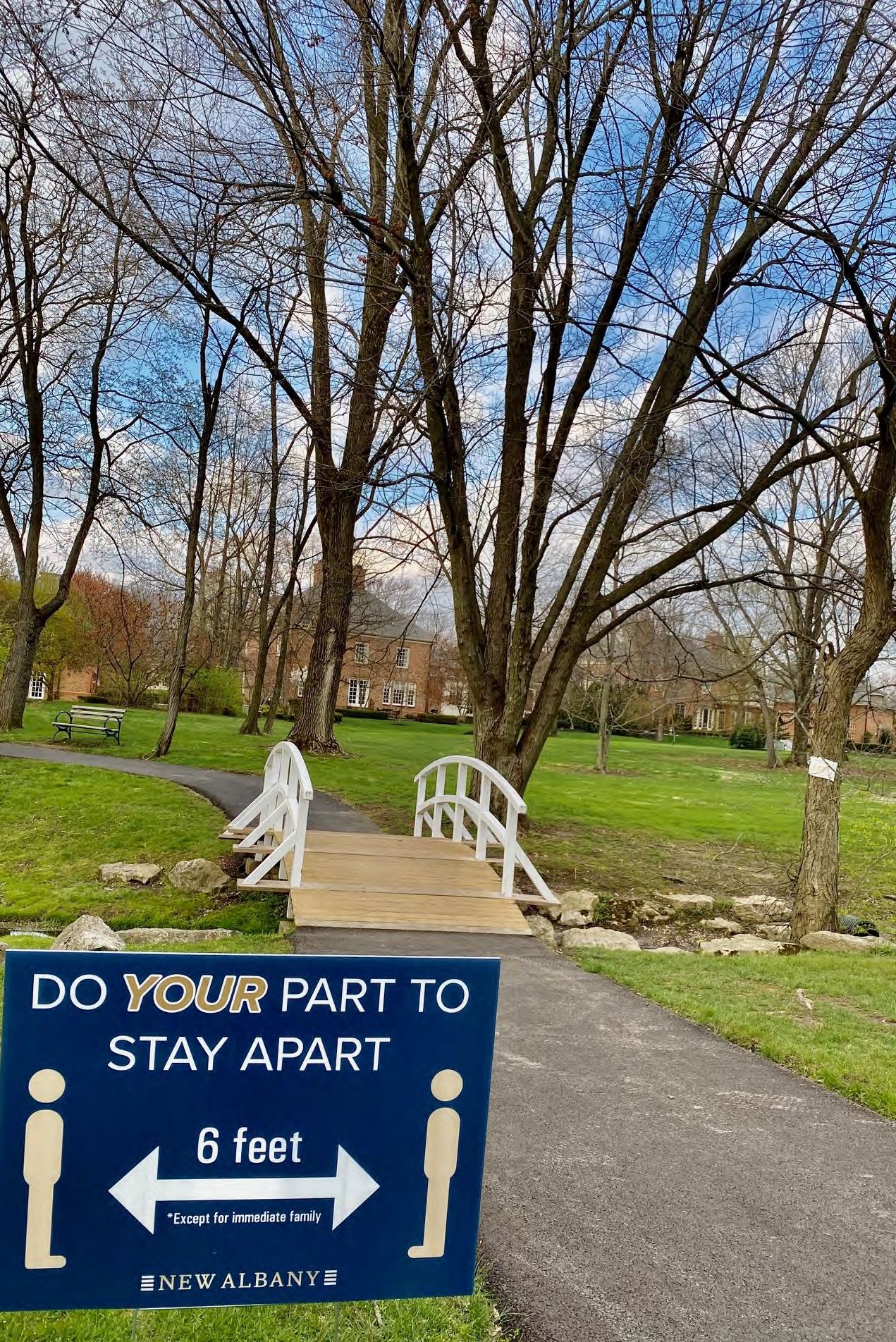 Paved walking trail leading to a white arched pedestrian bridge amid bare trees.