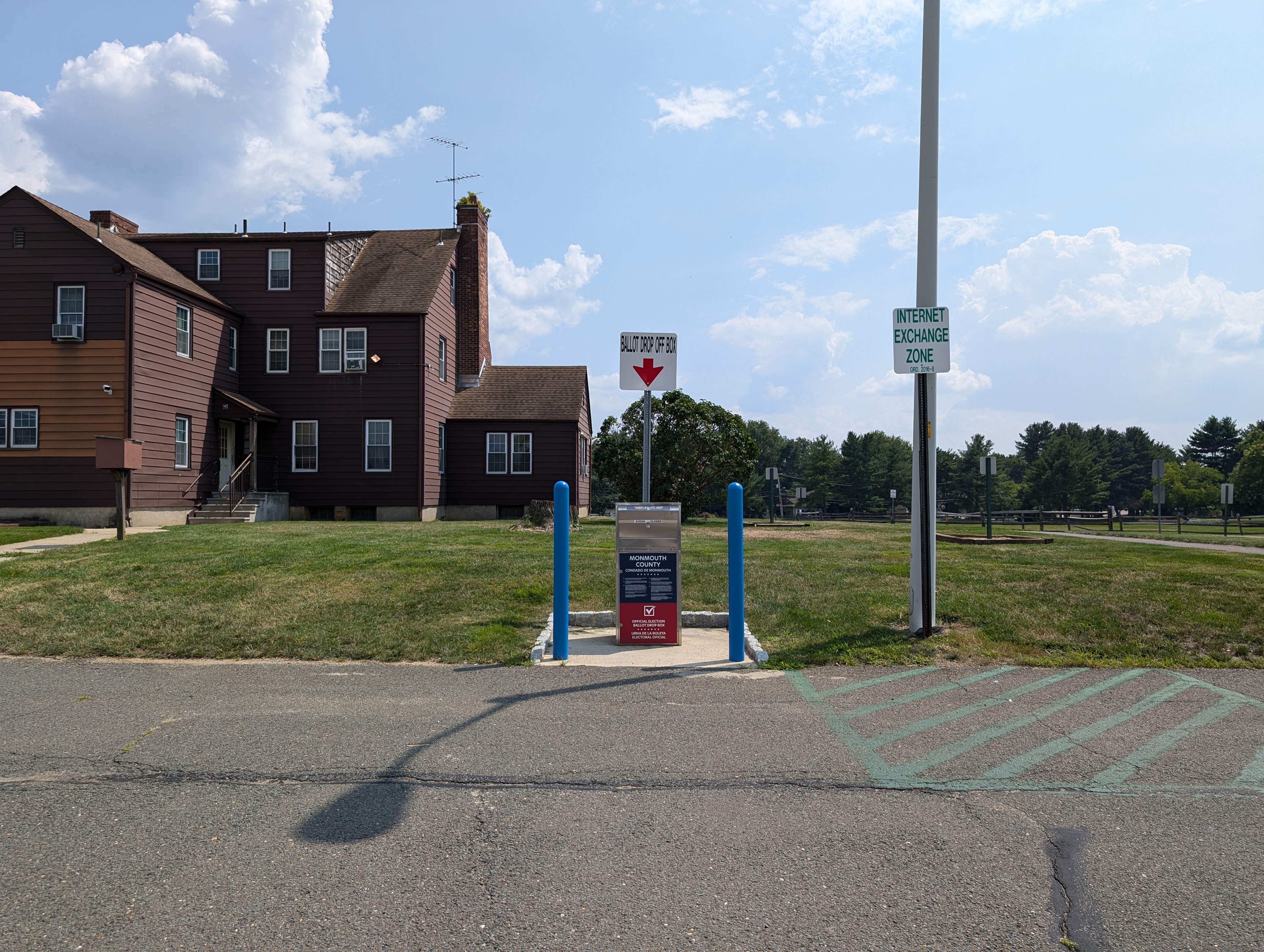 Secure metal ballot drop box with blue bollards in a parking lot outside a building.